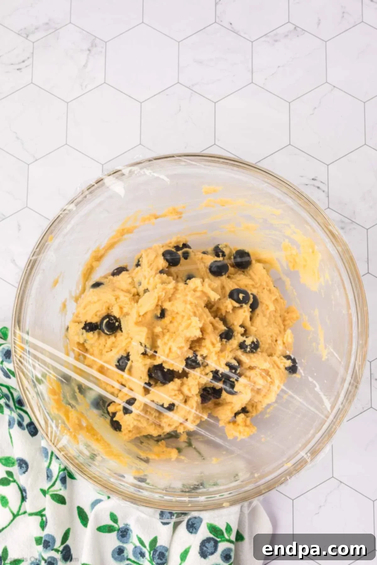 A bowl of cookie dough covered with plastic wrap, chilling in the refrigerator.