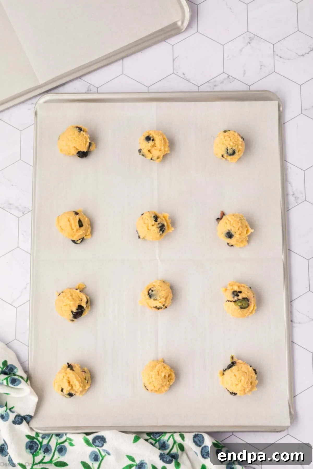 Scoops of lemon blueberry cookie dough spaced out on a baking sheet lined with parchment paper, ready for baking.