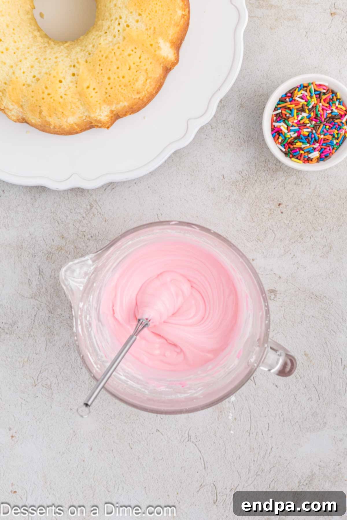 A vibrant pink glaze, made from powdered sugar, heavy cream, and food coloring, mixed smoothly in a small white bowl.