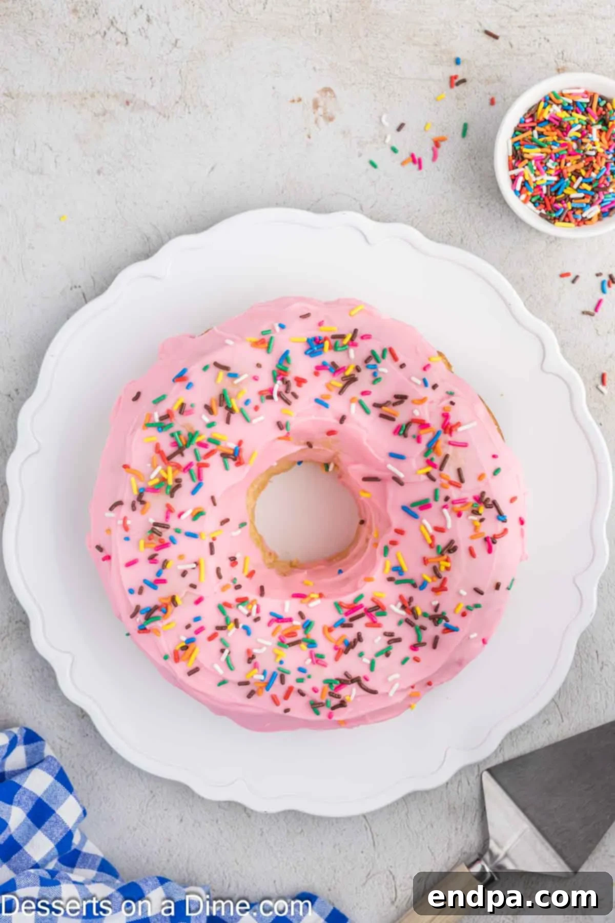 A finished Donut Cake, generously covered with pink glaze and adorned with colorful sprinkles, sitting majestically on a platter.