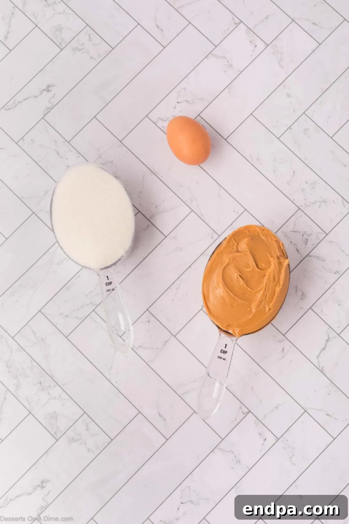 A bowl of creamy peanut butter, a bowl of granulated sugar, and a single egg are displayed as the three simple ingredients for cookies.