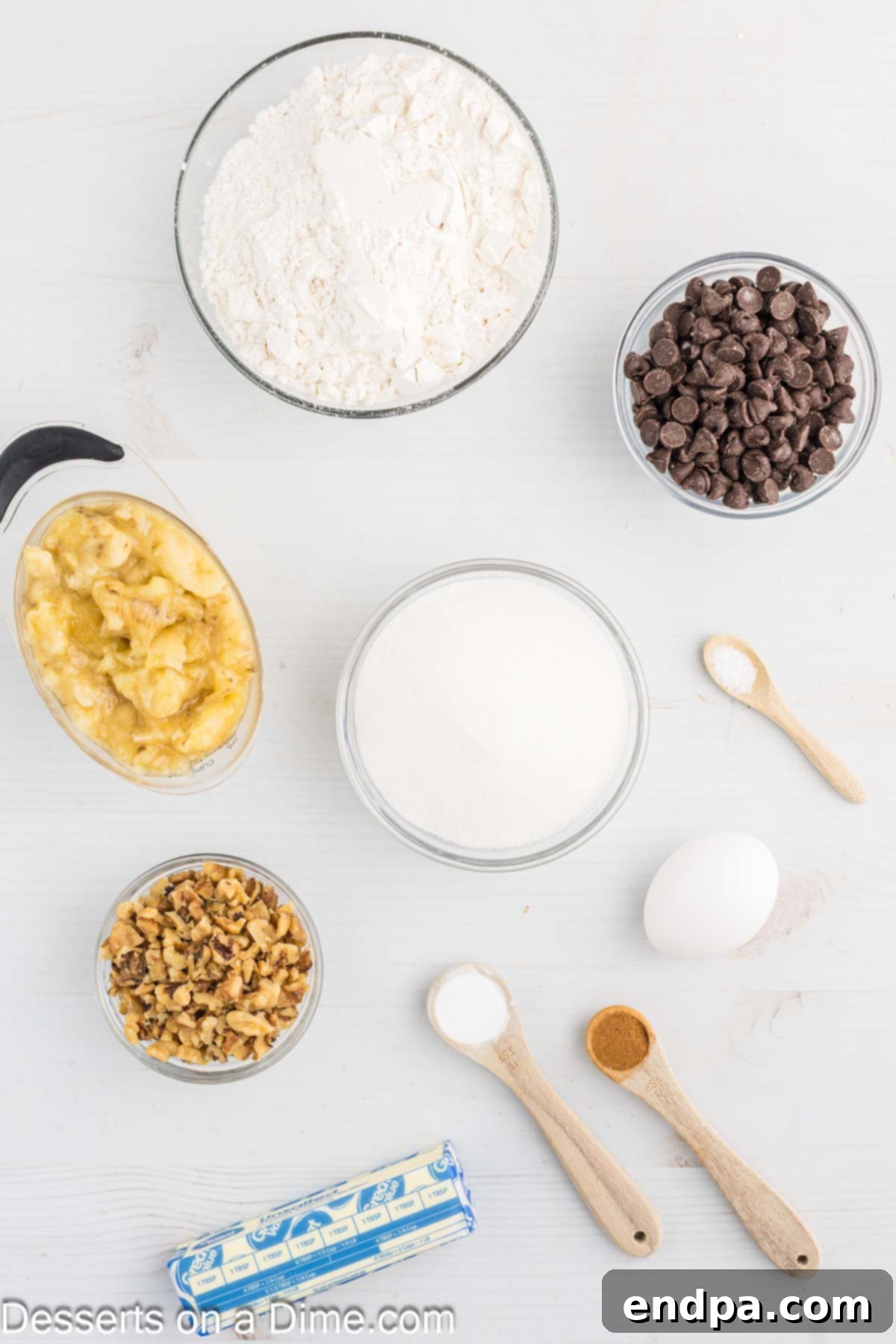 All the ingredients neatly laid out for making Banana Cookies: mashed bananas, softened butter, granulated sugar, an egg, baking soda, all-purpose flour, a pinch of salt, ground cinnamon, chocolate chips, and chopped walnuts.