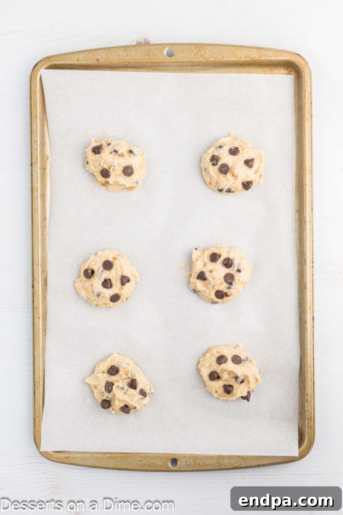 Balls of banana cookie dough scooped onto a parchment-lined baking sheet, ready for the oven.