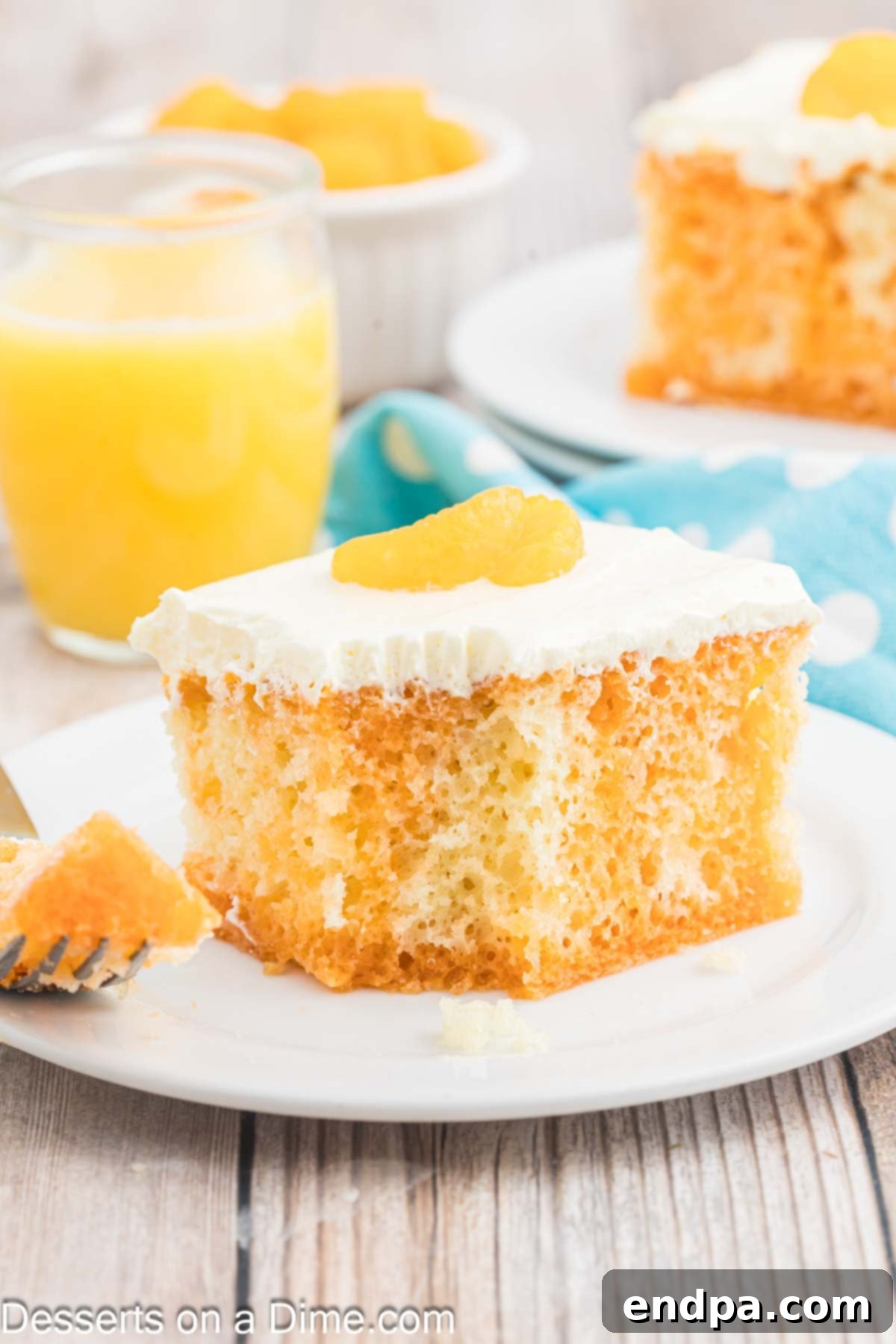 Velvet Orange Dream Cake 2 Slice of vibrant Orange Creamsicle Cake on a white plate, showcasing its moist orange base and creamy white topping, garnished with fresh mandarin oranges.