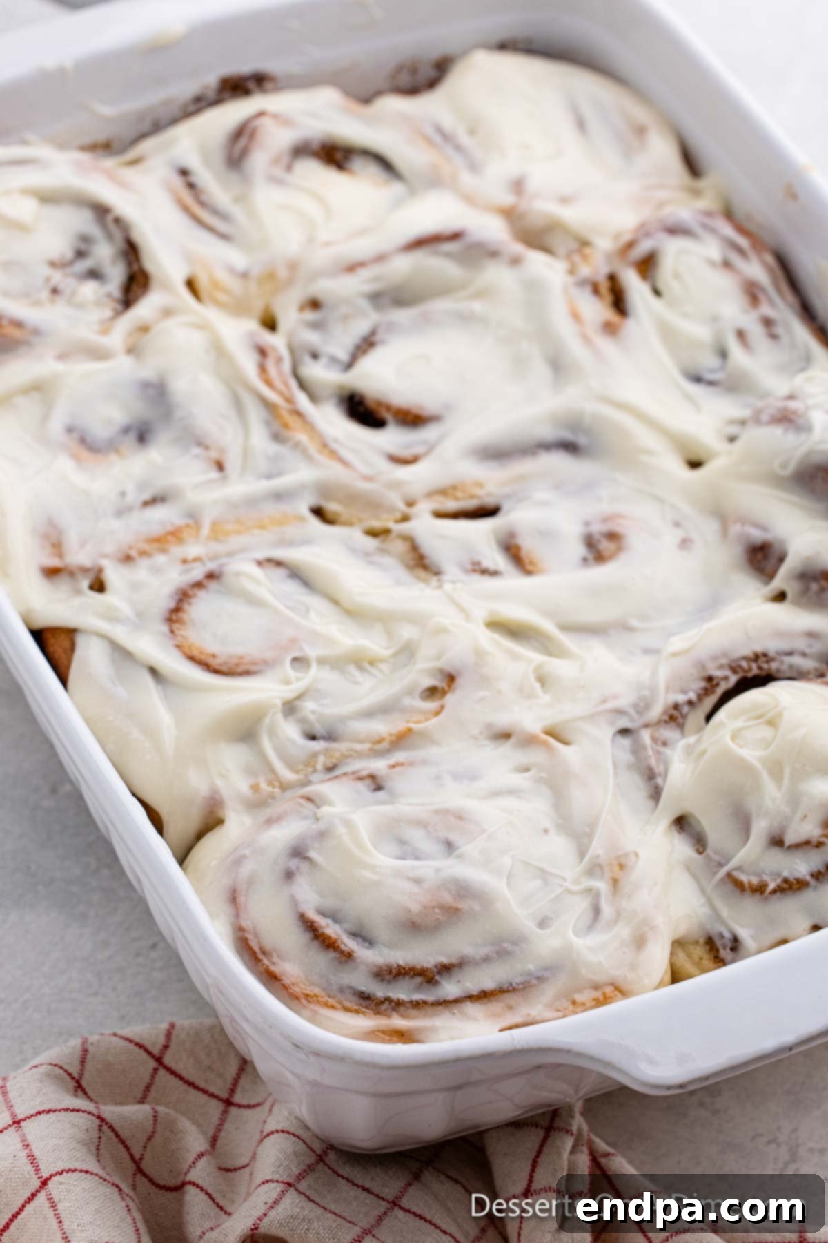 A baking dish filled with golden-brown homemade cinnamon rolls, lavishly coated in a smooth cream cheese icing.