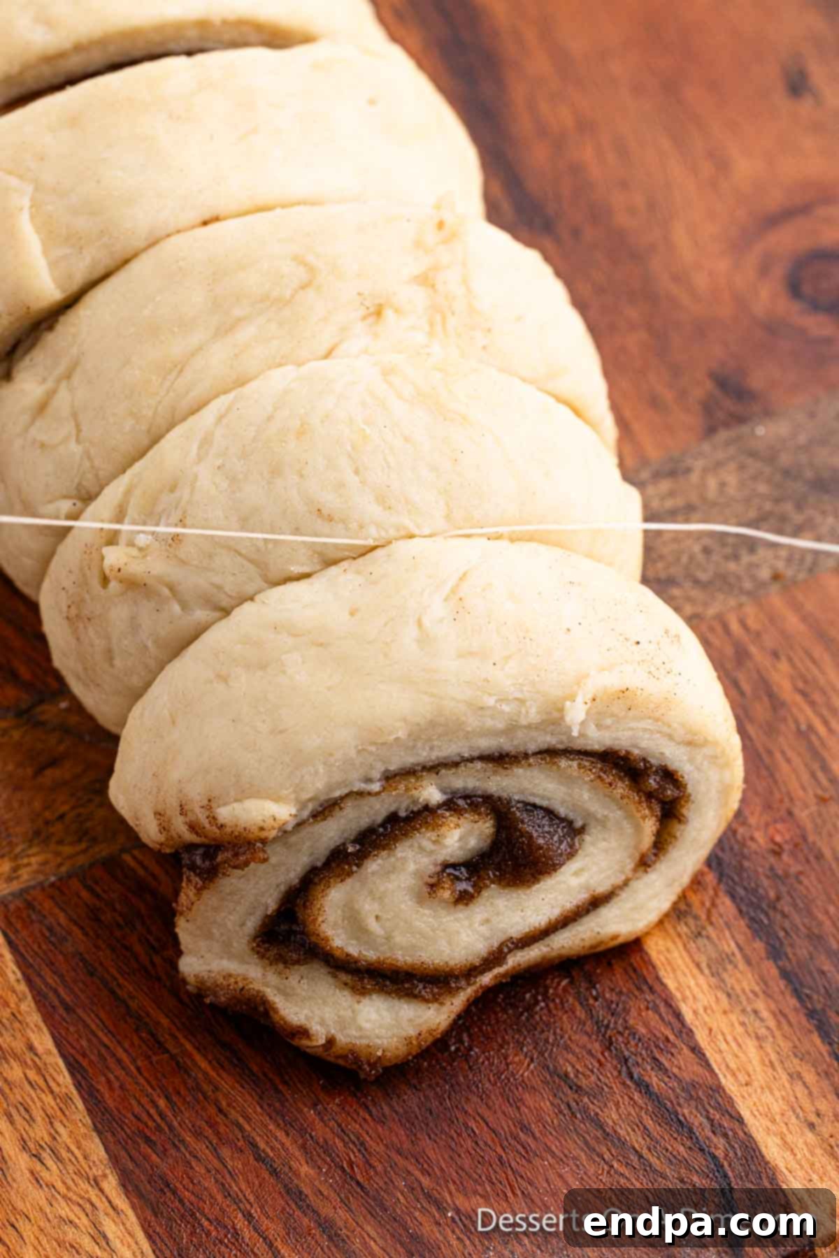 The rolled dough log being cut into individual cinnamon rolls using a piece of dental floss for clean edges.