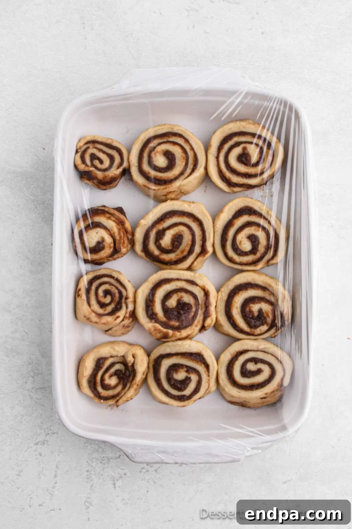 Sliced cinnamon rolls arranged closely together in a glass baking dish, waiting for their final rise.