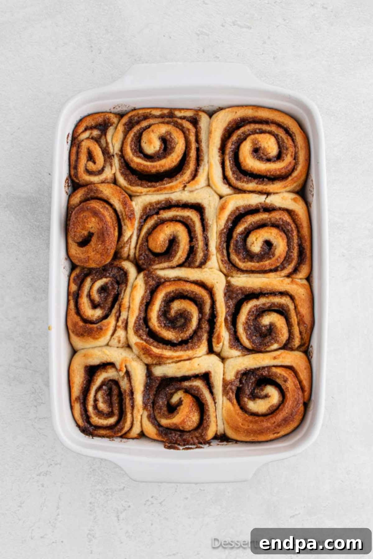 Baked cinnamon rolls cooling slightly in the baking dish, steam gently rising.