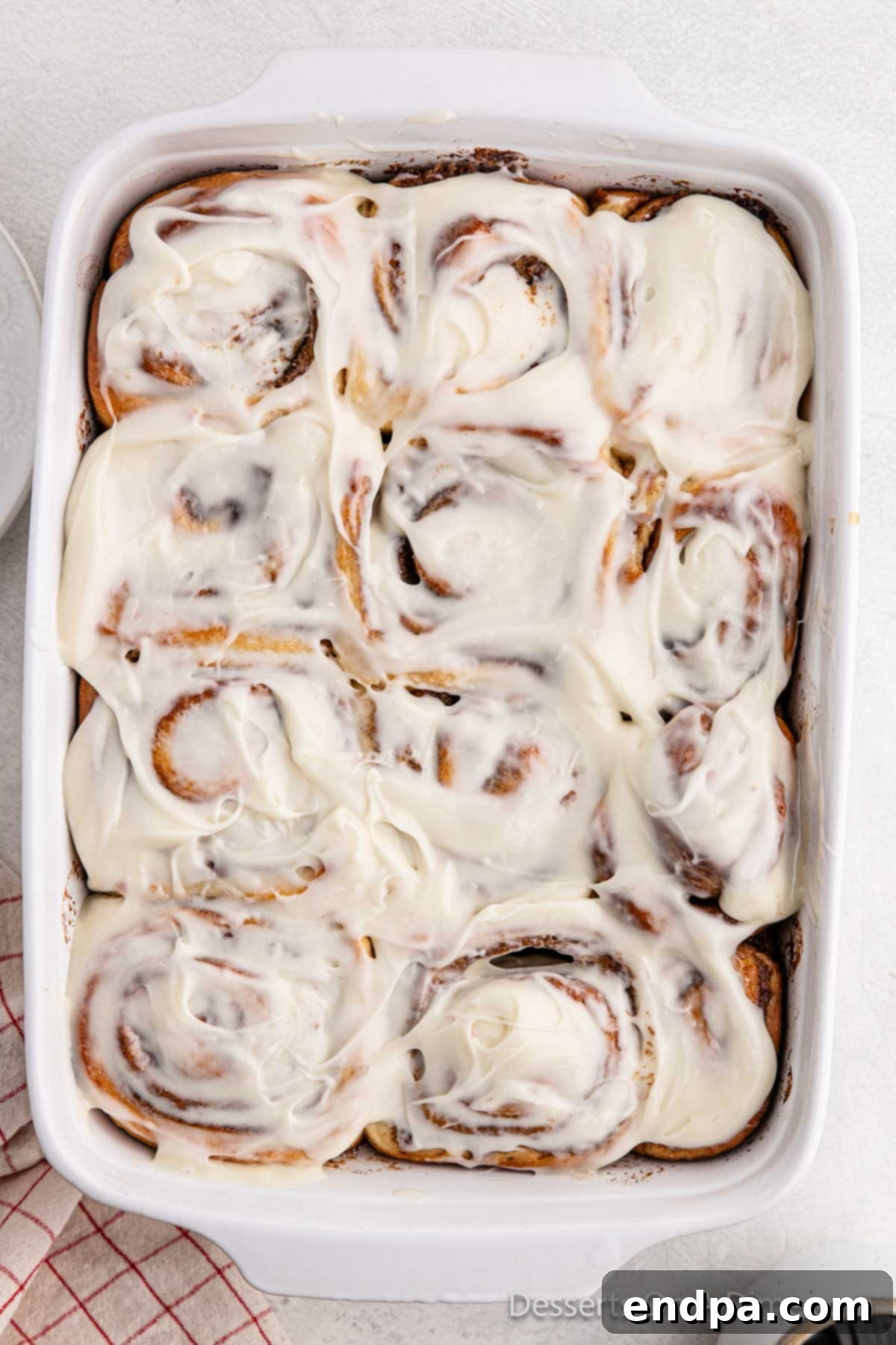 Warm, freshly baked cinnamon rolls in a dish, glistening with a generous layer of cream cheese icing, ready to be served.