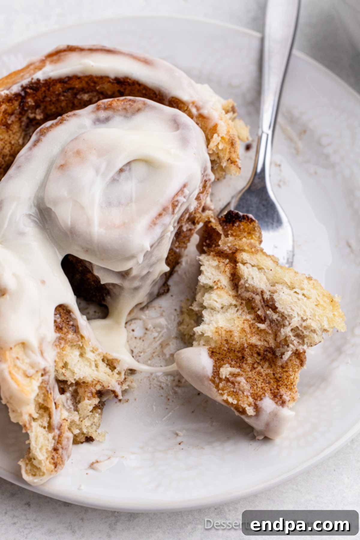 A single homemade cinnamon roll placed on a white ceramic plate, beautifully iced and ready to be enjoyed.