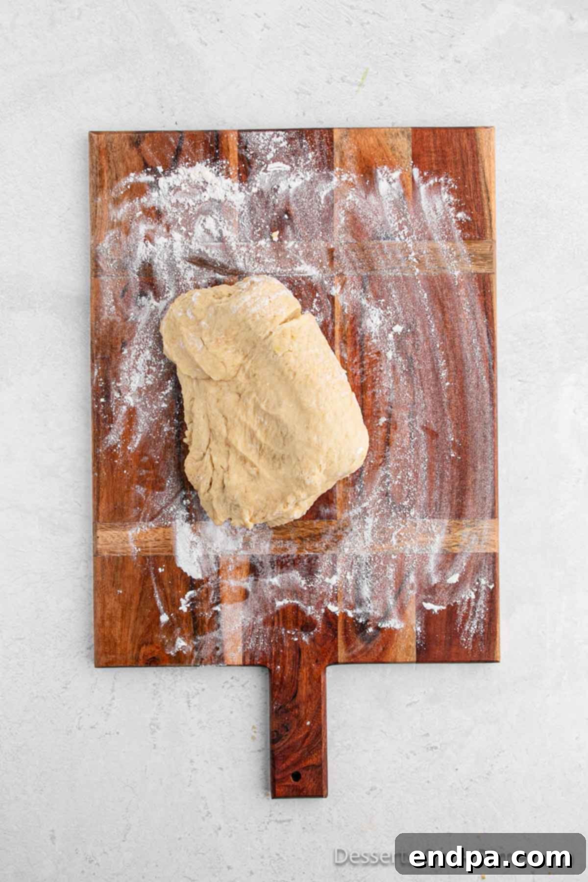 Dough on a lightly floured cutting board, flattened and ready to be rolled into a large rectangle.