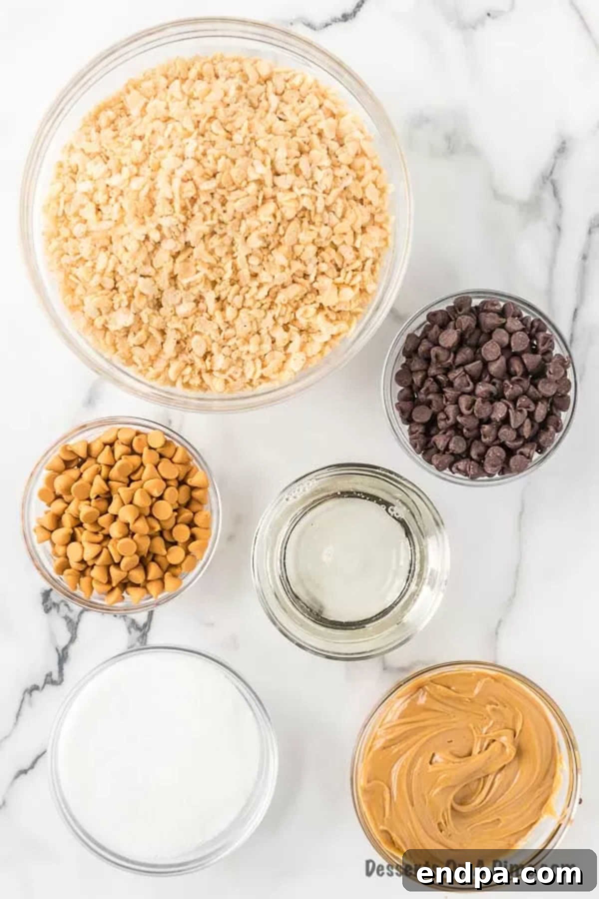 A flat lay arrangement of all the necessary ingredients for Scotcheroos: a bowl of Rice Krispies cereal, a jar of creamy peanut butter, a bag of granulated sugar, a bottle of light corn syrup, a bowl of semi-sweet chocolate chips, and a bowl of butterscotch chips.