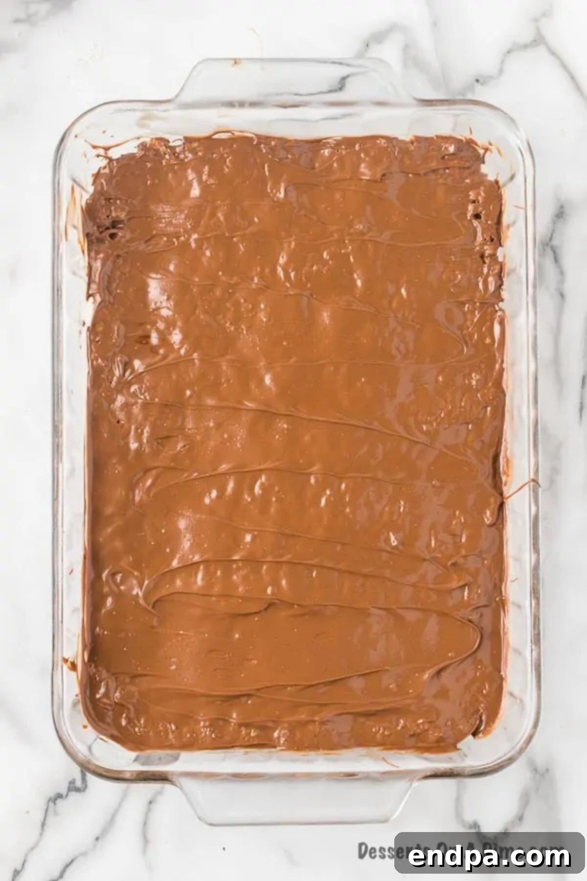 A 9x13 inch baking pan with the Rice Krispies and peanut butter base, now covered with a smooth, perfectly glossy layer of melted chocolate and butterscotch topping, ready to set.