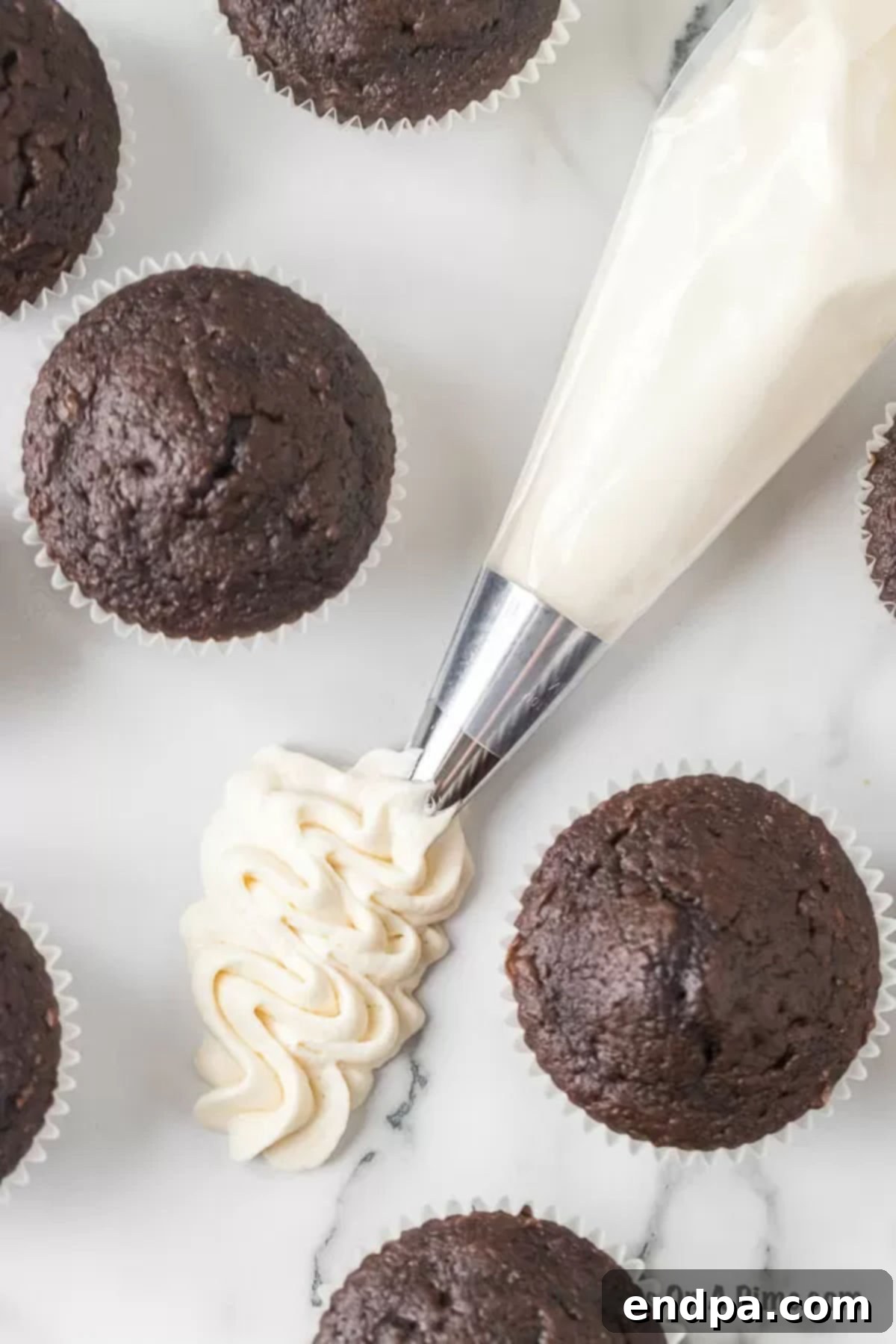 Piping bag filled with marshmallow frosting next to decorated chocolate cupcakes, ready for serving.