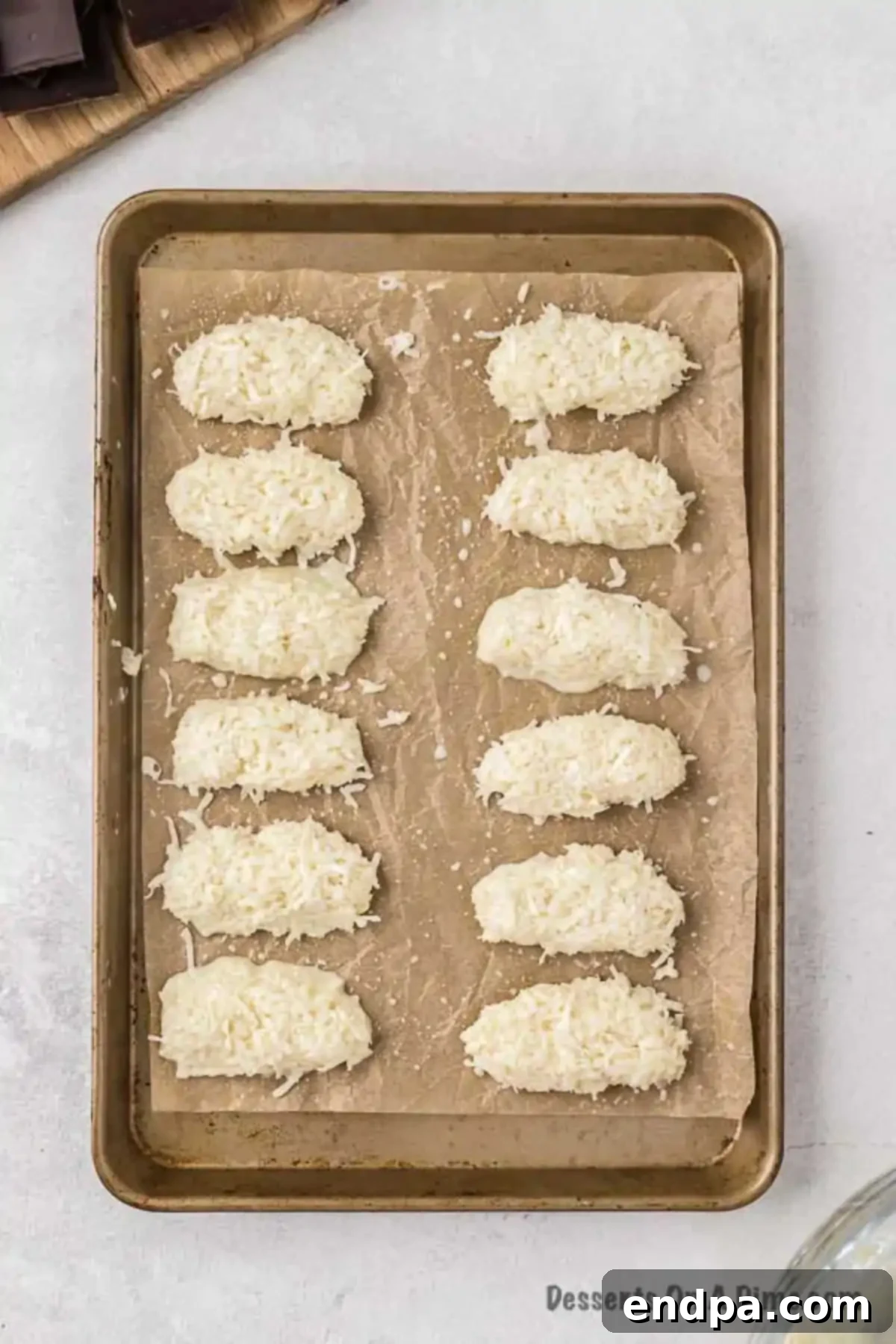 Decadent Homemade Mounds Bars 6 Shaped coconut mounds on a baking sheet, ready for the freezer.