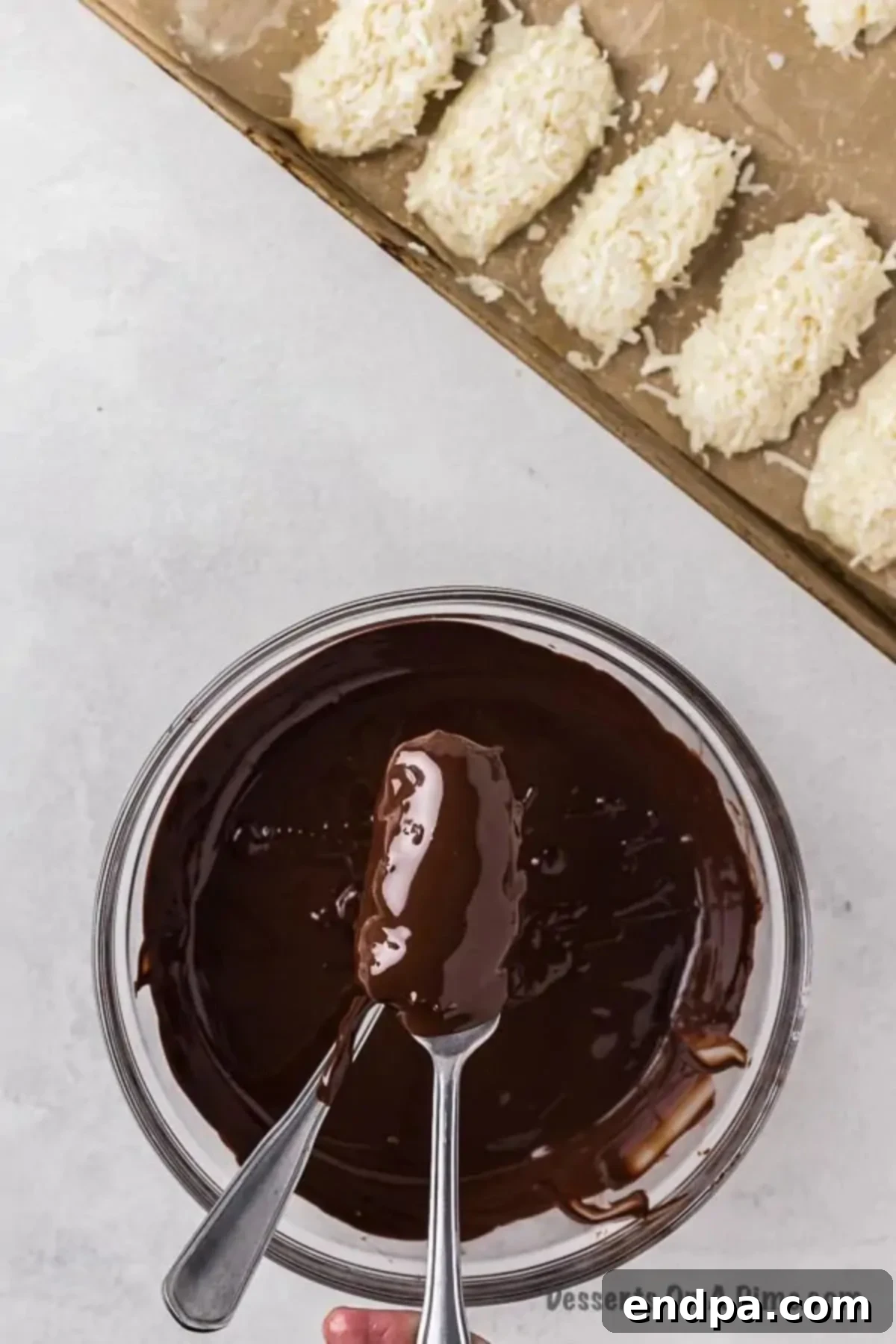 Decadent Homemade Mounds Bars 9 A coconut mound being dipped into melted chocolate using two forks.