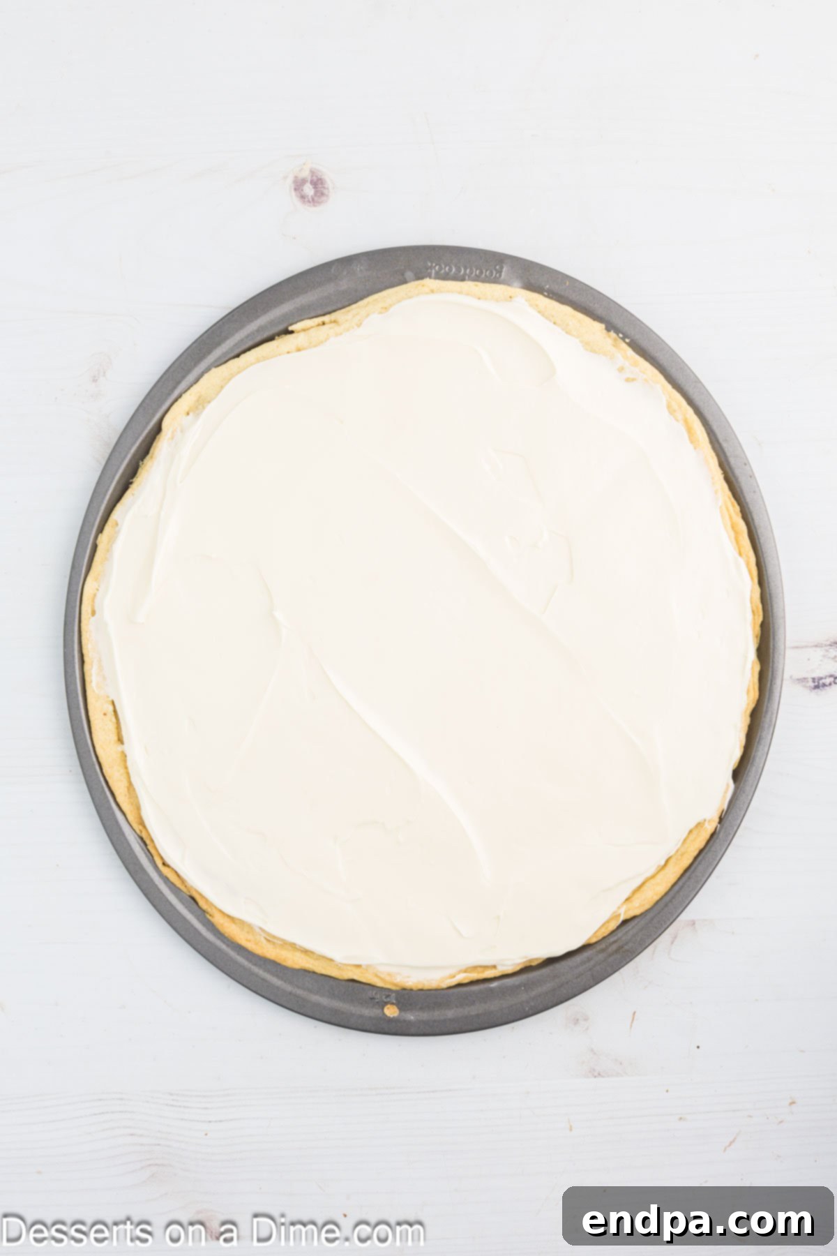 Fresh Fruit Fiesta Pizza 6 The fluffy cream cheese frosting being spread smoothly and evenly over the cooled sugar cookie crust.