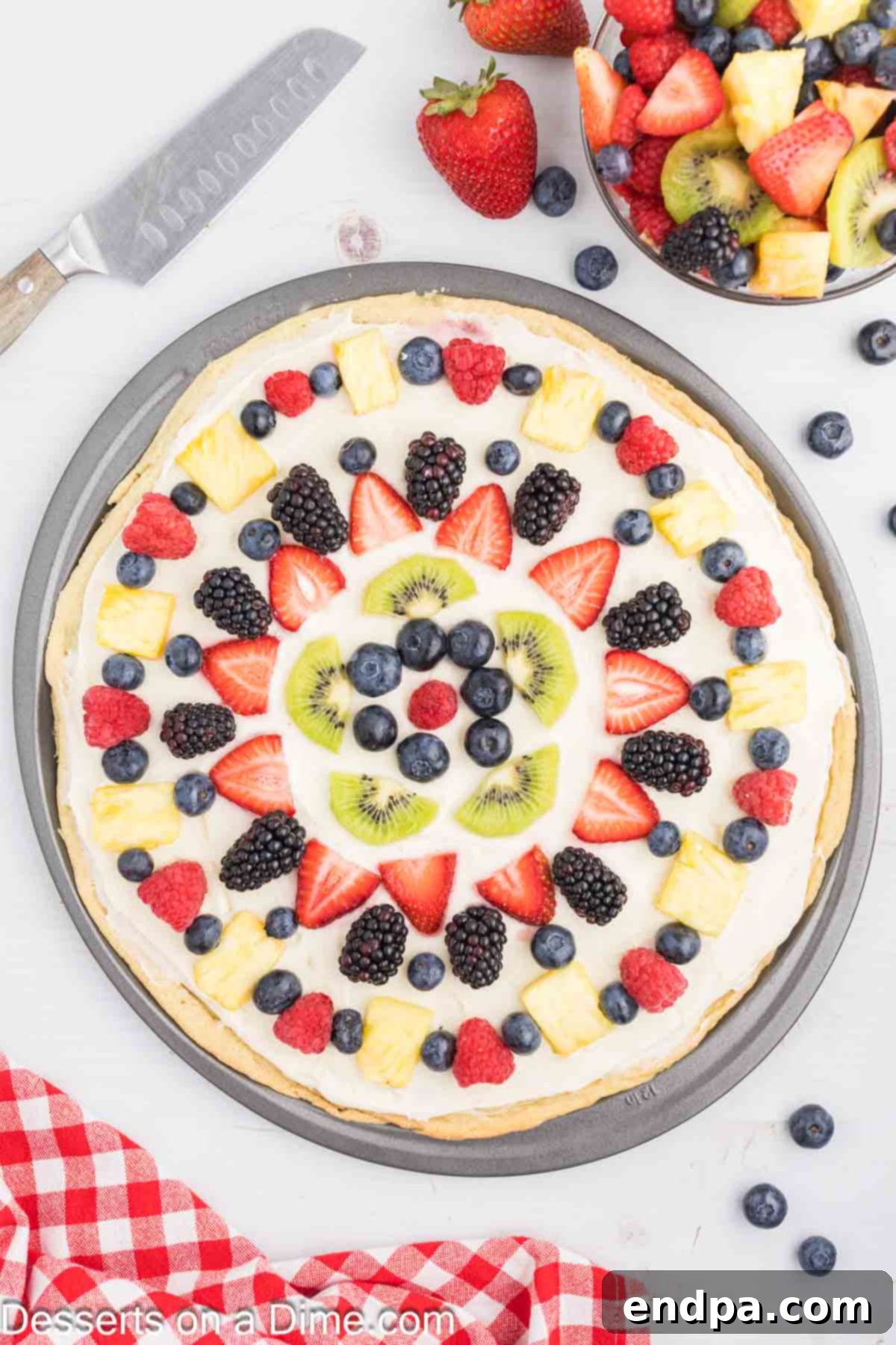 Fresh Fruit Fiesta Pizza 7 Assorted fresh fruits like strawberries, blueberries, kiwi, and pineapple slices beautifully arranged on top of the cream cheese frosting layer of the fruit pizza.