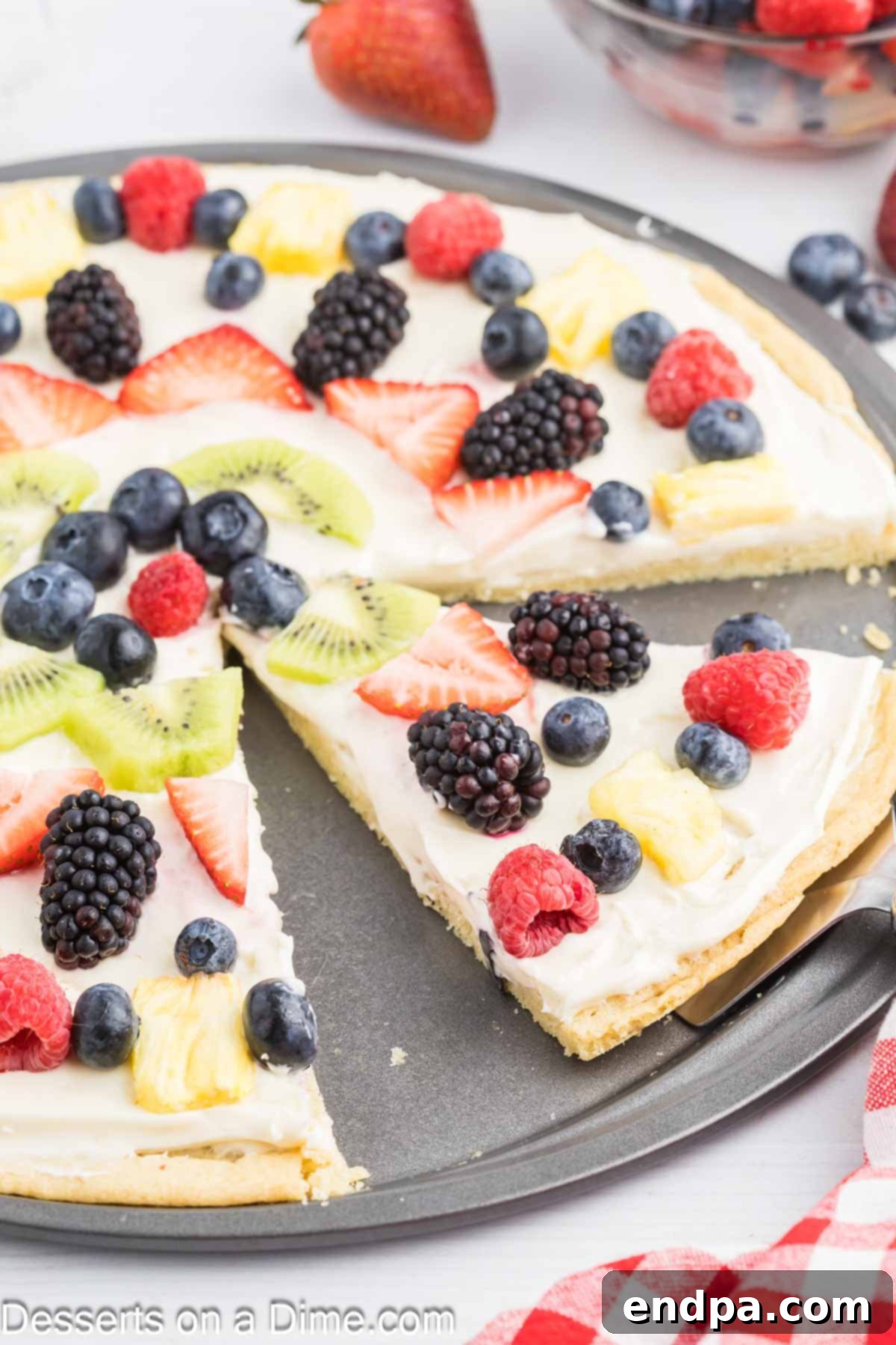 Fresh Fruit Fiesta Pizza 8 A hand using a pizza cutter to slice a finished Fruit Pizza, revealing its layers of sugar cookie crust, cream cheese frosting, and colorful fresh fruit toppings.