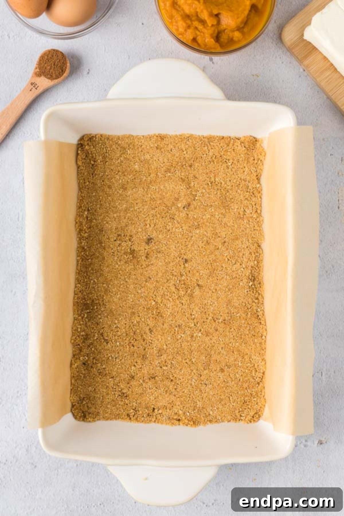 Spiced Pumpkin Cheesecake Bars 5 The graham cracker crust mixture pressed into the bottom of a 9X13 baking dish lined with parchment paper.