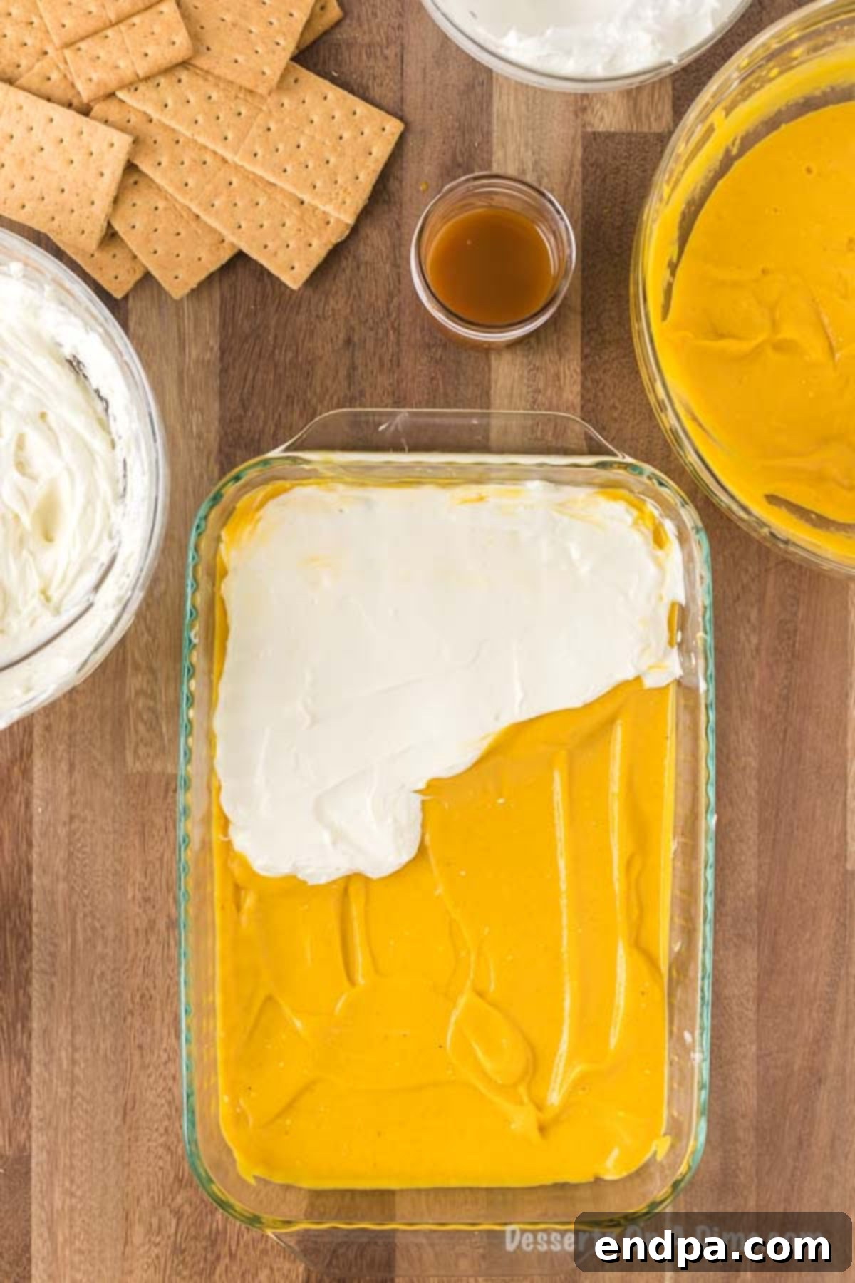 Half of the remaining cream cheese mixture is being spread smoothly over the pumpkin pudding layer in the baking pan, creating another distinct creamy stratum for the pumpkin lasagna.