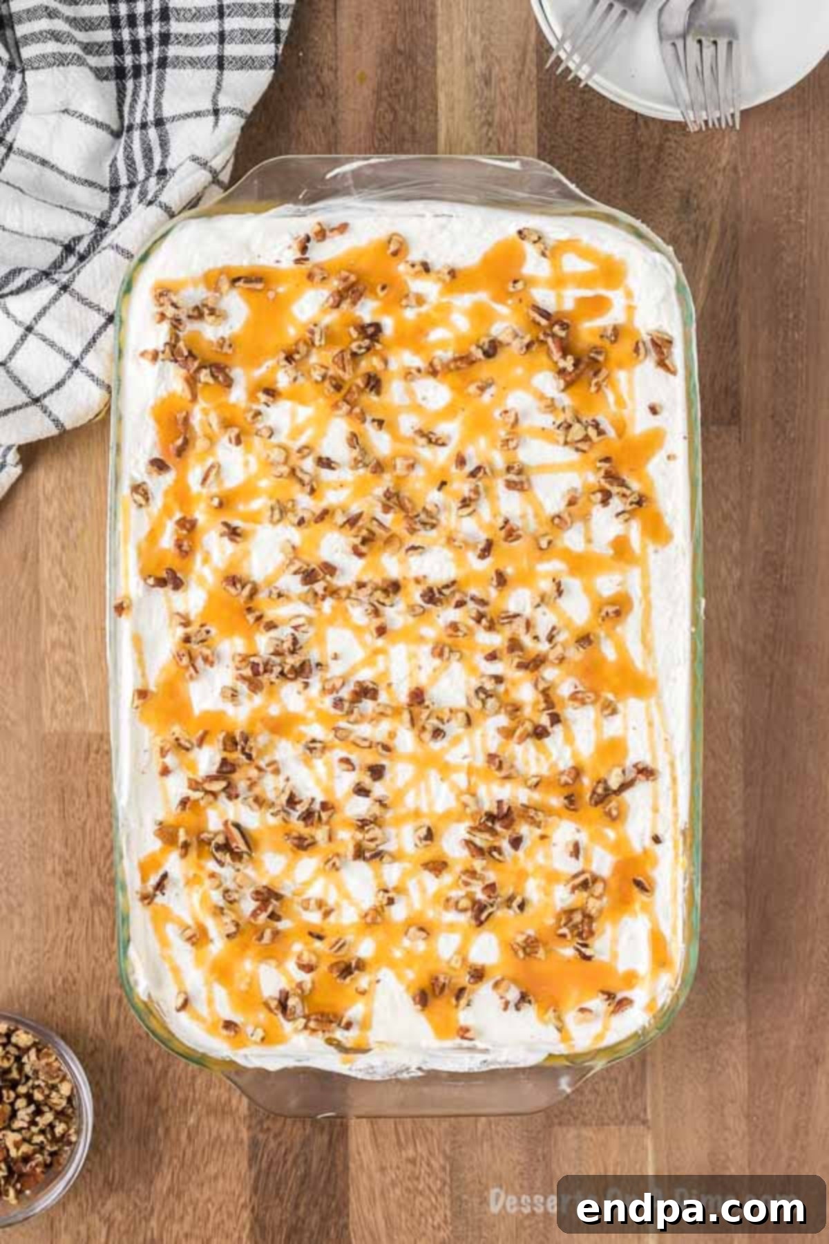 The finished pumpkin lasagna rests in the baking pan, beautifully topped with a generous layer of cool whip, artistically drizzled with caramel sauce, and sprinkled with chopped pecans, ready to be chilled and served.
