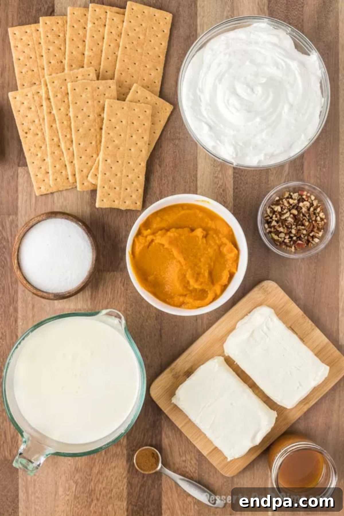 A flat lay photograph showcasing all the ingredients required to make Pumpkin Lasagna: graham crackers, softened cream cheese, granulated sugar, milk, whipped topping, vanilla instant pudding mix, pumpkin puree, pumpkin pie spice, caramel sauce, and chopped pecans, arranged neatly on a surface.