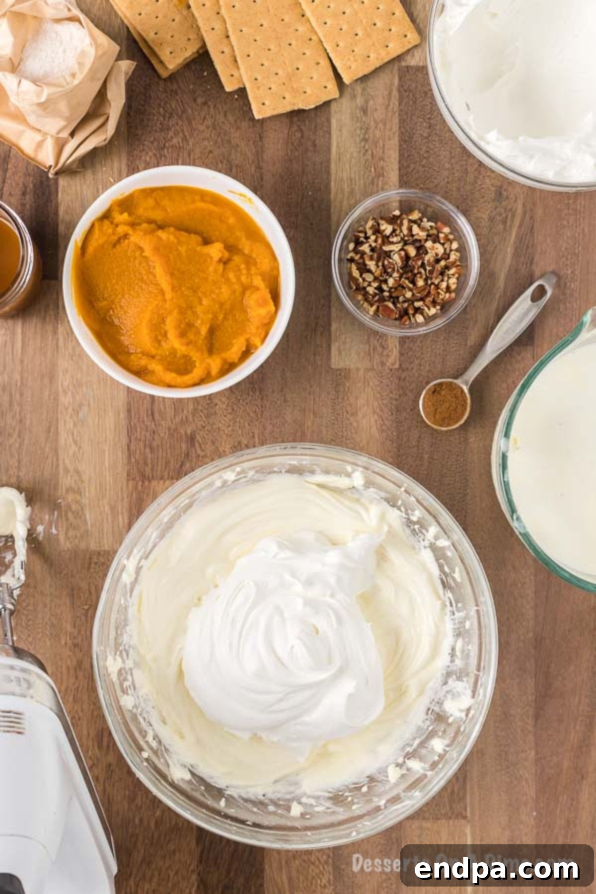 A generous dollop of cool whip is being added to the mixed cream cheese and milk mixture in a large bowl, preparing for the final blend of the first creamy layer.