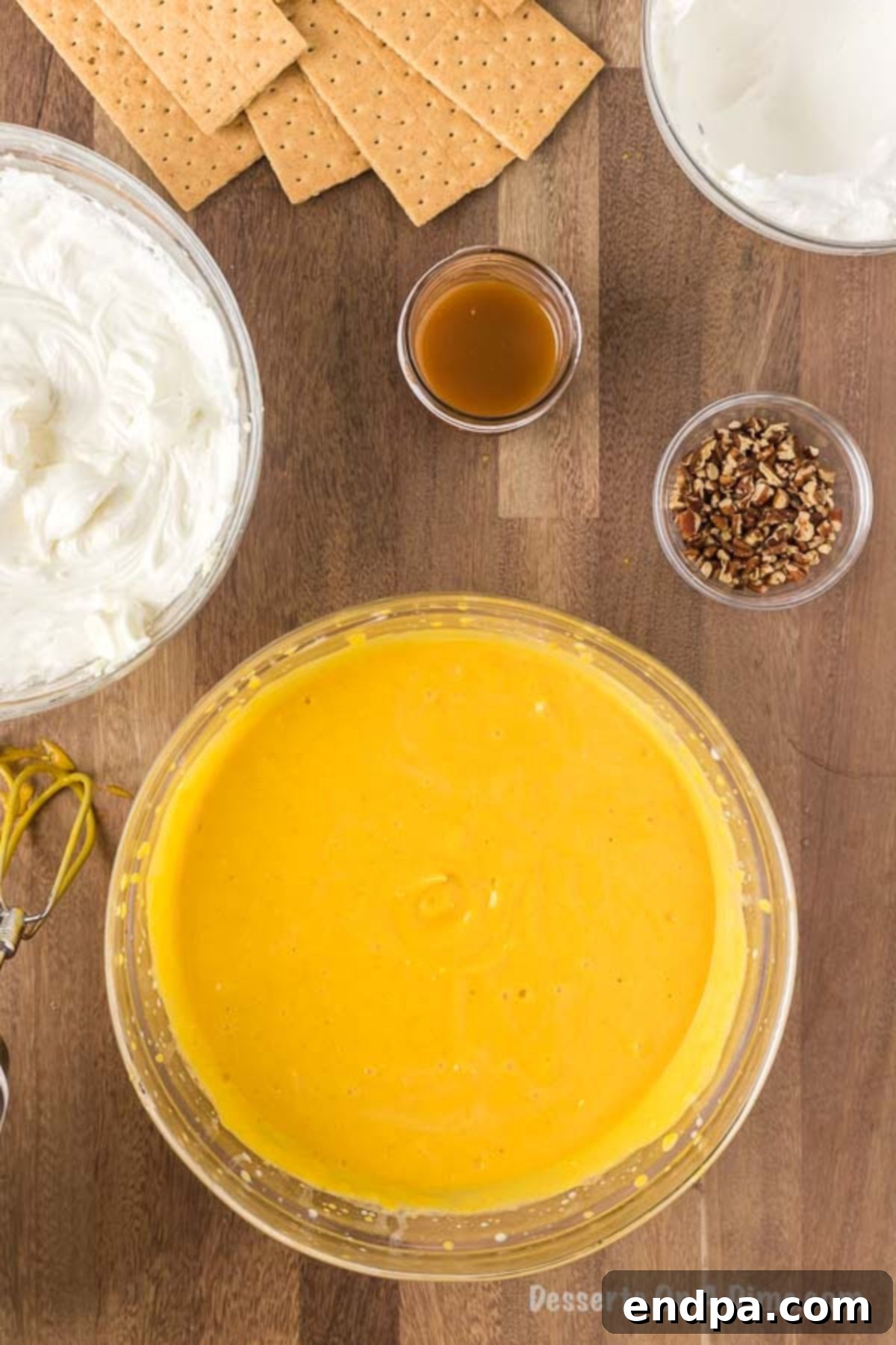 Pumpkin puree, cold milk, and pumpkin pie spice are being vigorously whisked together in a large mixing bowl, forming a smooth, aromatic pumpkin pudding mixture for the dessert lasagna.