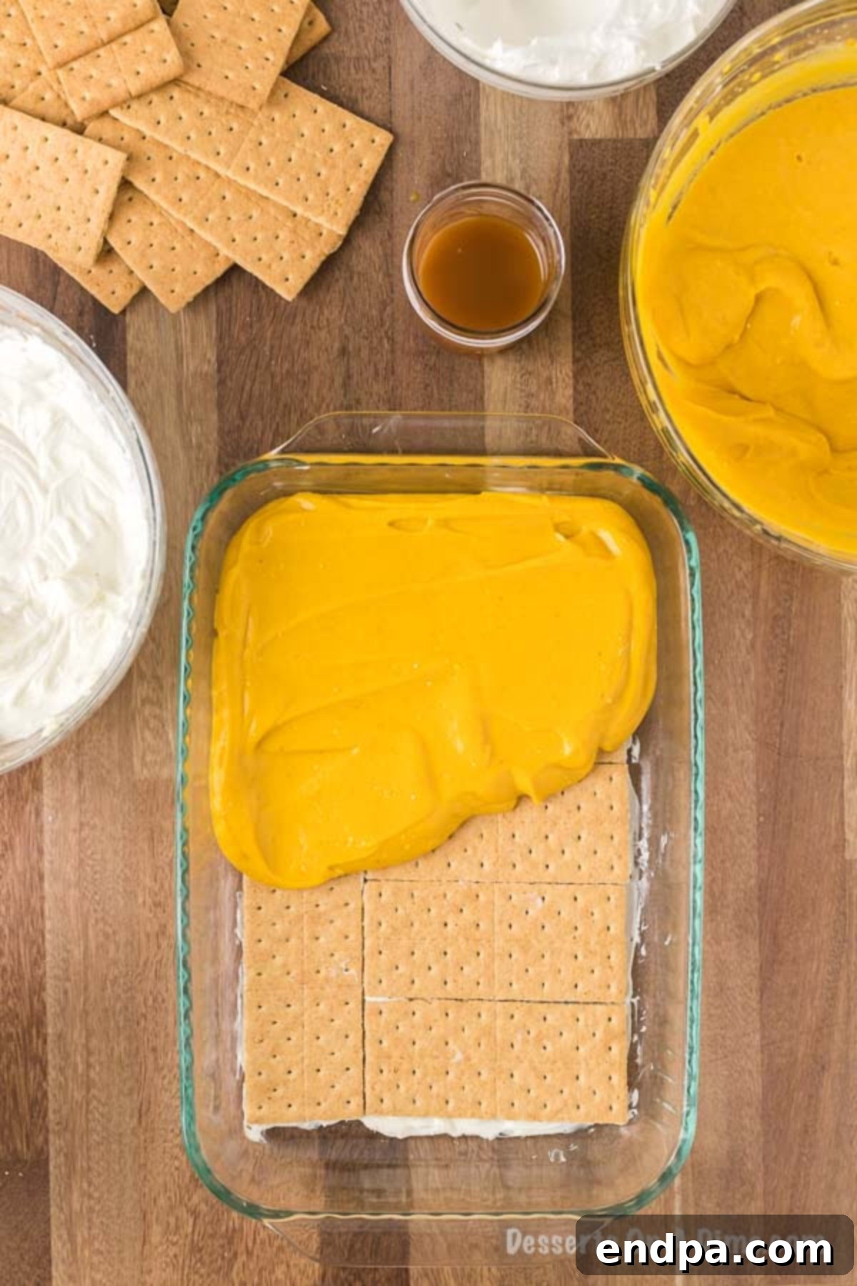 Half of the creamy pumpkin pudding mixture is being carefully spread over the layer of graham crackers in the 9x13 inch baking pan, ensuring an even distribution for the next layer of the pumpkin lasagna.