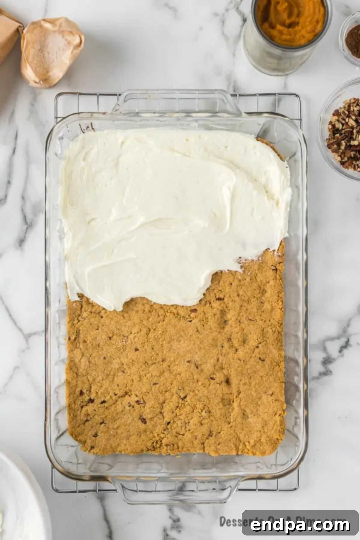 Spreading the smooth cream cheese mixture evenly over the cooled graham cracker crust in the baking dish.