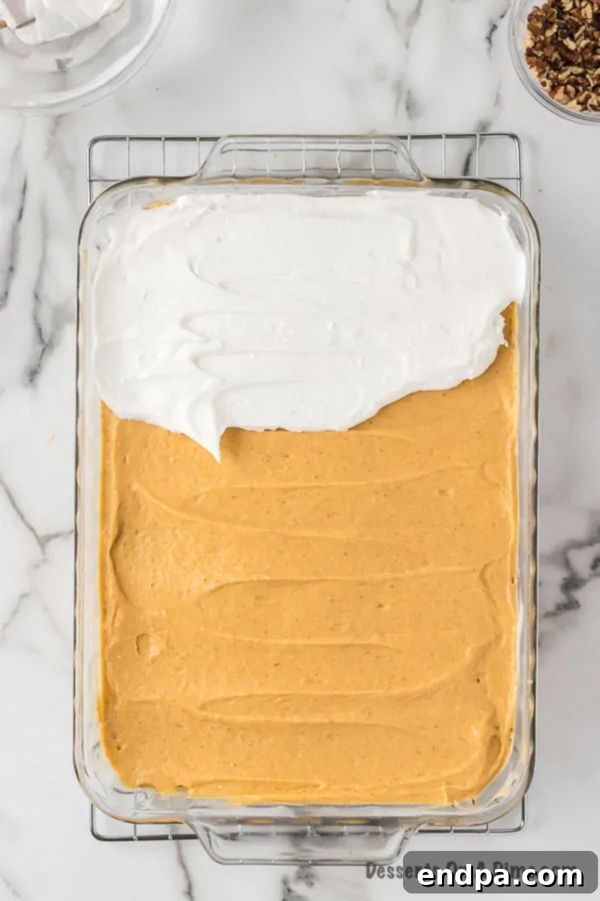 Spreading the pumpkin mixture over the cream cheese layer, then topping with the remaining whipped topping and chopped pecans to finish the Pumpkin Delight.