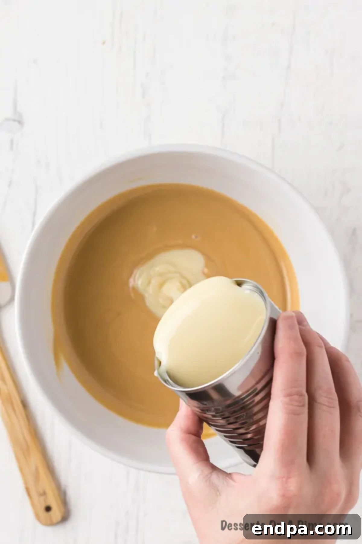 Sweetened condensed milk being poured into the melted chocolate and peanut butter mixture.