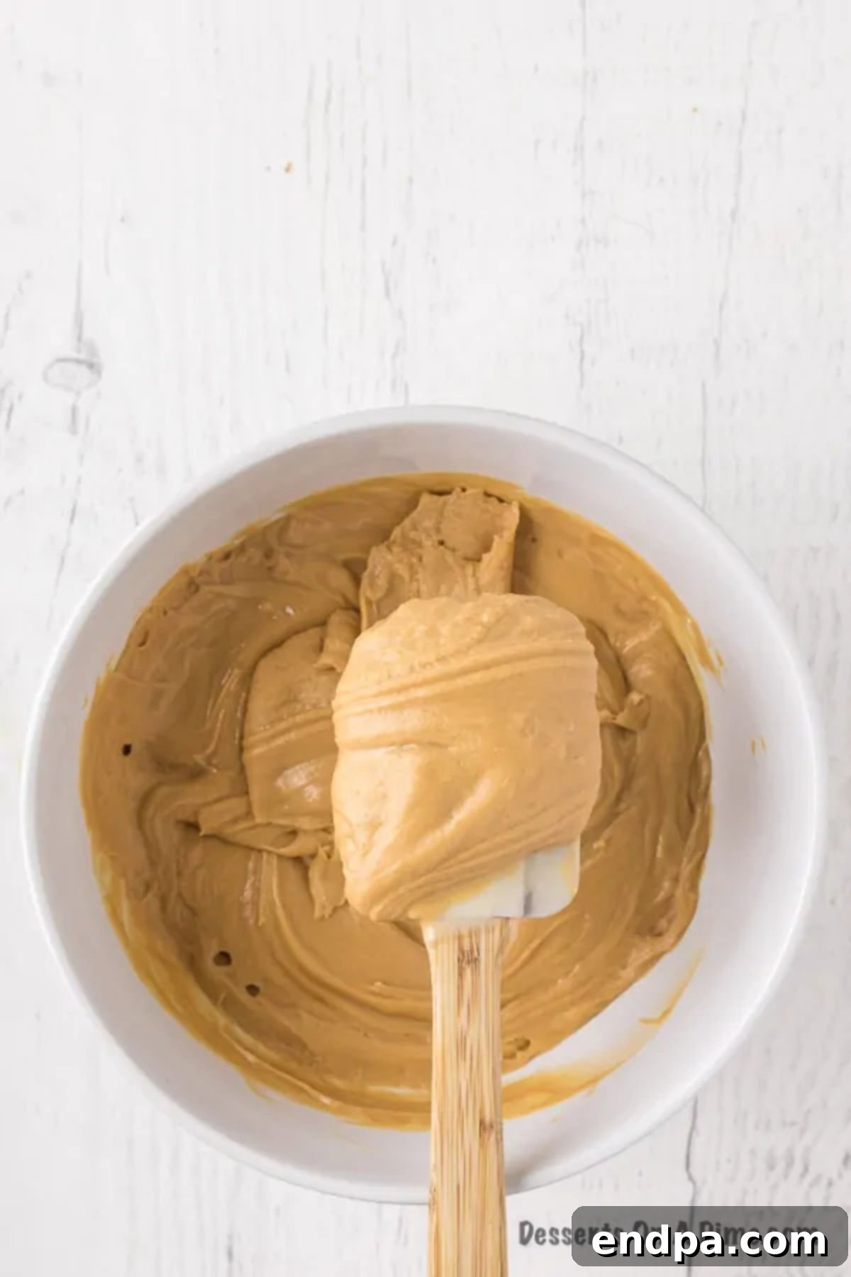 A spatula scraping the thoroughly combined fudge mixture in the bowl.