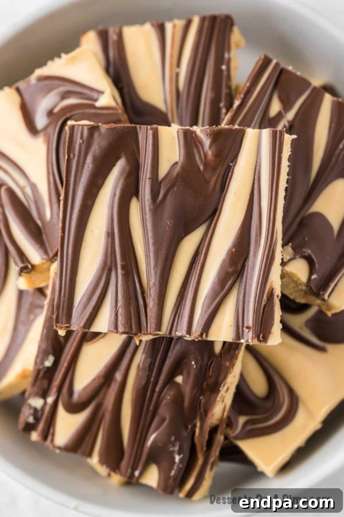 Tiger butter fudge cut into squares stacked in a bowl, showcasing its beautiful swirls of chocolate and peanut butter