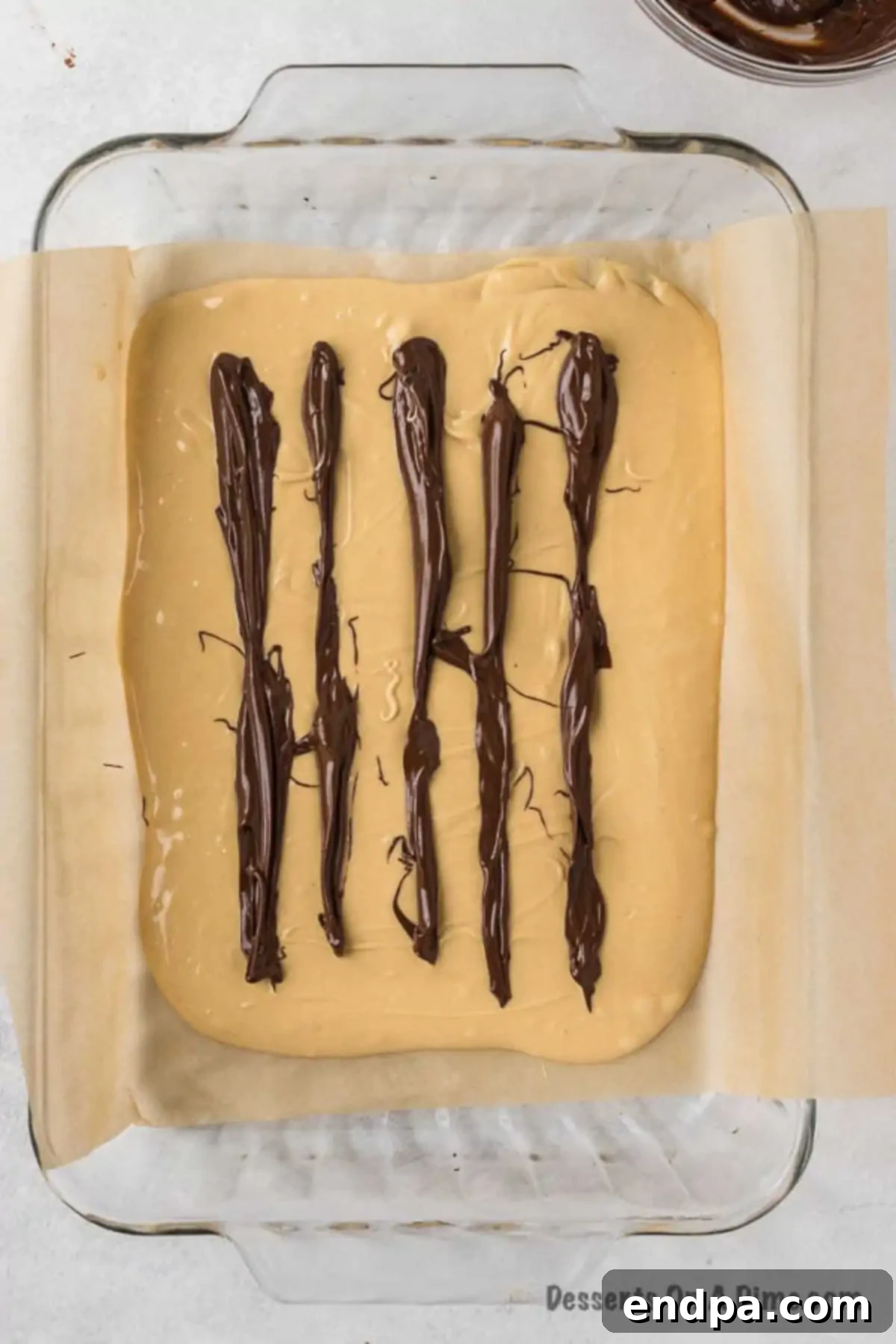Drizzling melted semi-sweet chocolate in parallel lines over the peanut butter base