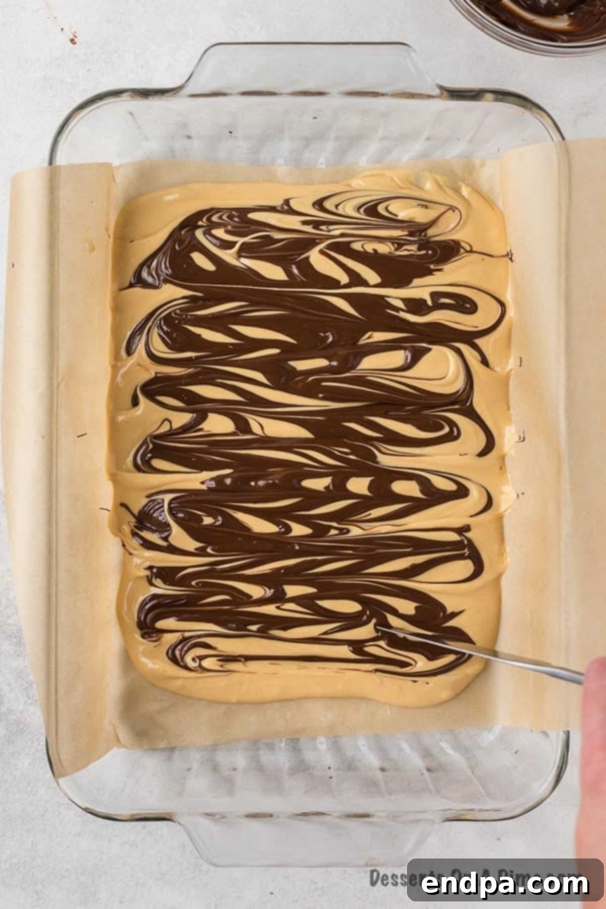 Using a long knife to swirl the melted chocolate into the peanut butter mixture for a marbled tiger effect