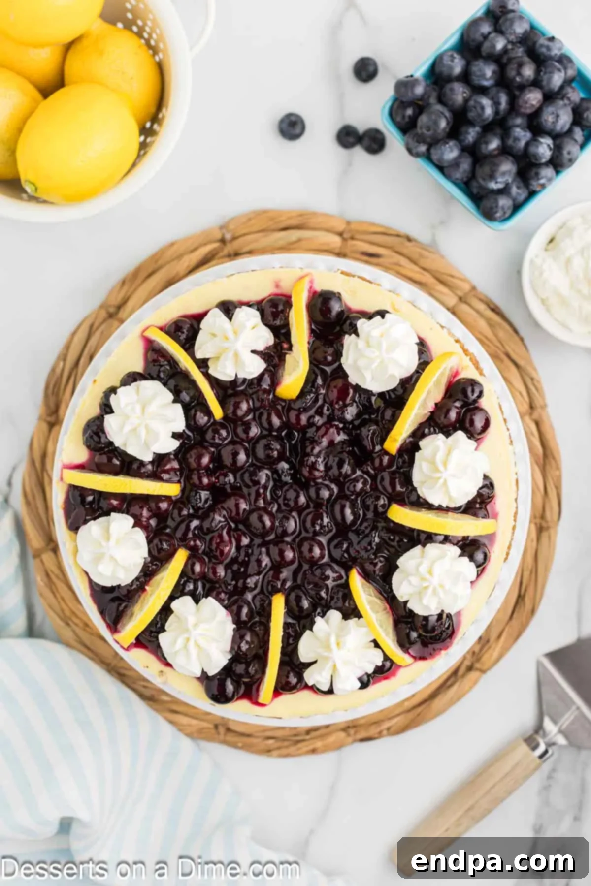 Heavenly Lemon Blueberry Cheesecake 11 A stunning Lemon Blueberry Cheesecake adorned with a generous layer of vibrant blueberry topping, fluffy whipped cream, and elegant fresh lemon slices, ready to be enjoyed.