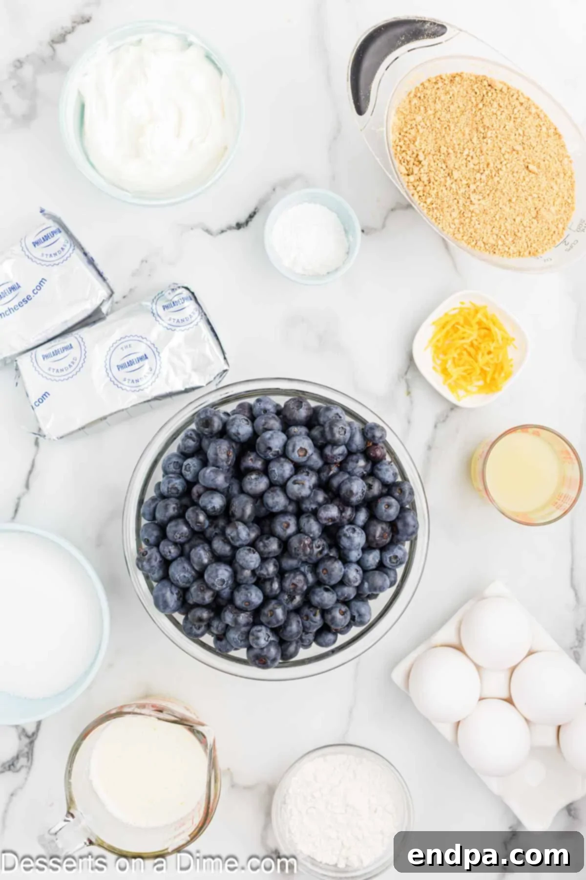 Heavenly Lemon Blueberry Cheesecake 3 A flat lay image displaying all the necessary ingredients for Lemon Blueberry Cheesecake, including graham cracker crumbs, sugar, unsalted butter, softened cream cheese, sour cream, fresh lemon juice and zest, eggs, and fresh blueberries.