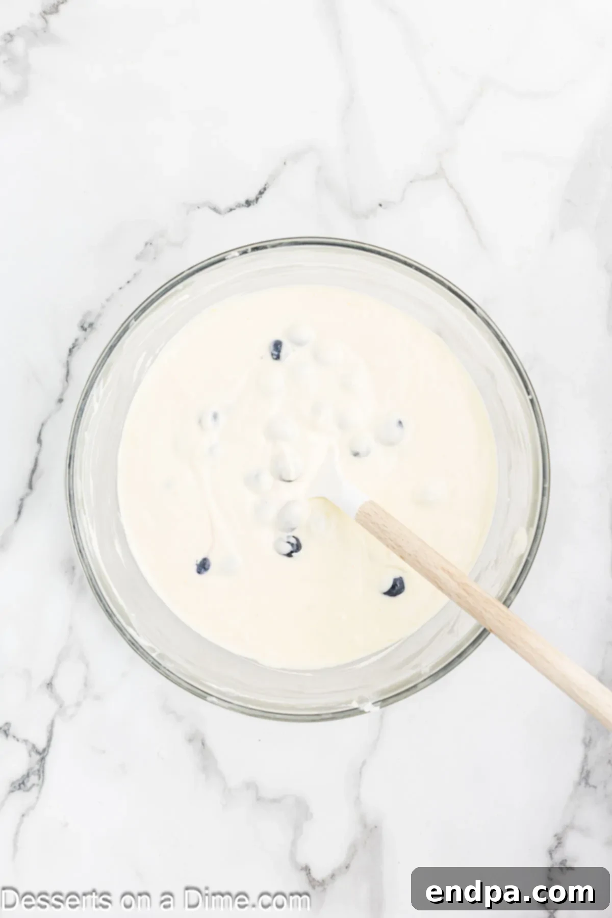 Heavenly Lemon Blueberry Cheesecake 6 Fresh blueberries are gently folded into the creamy cheesecake batter in a mixing bowl using a spatula, ensuring even distribution without crushing the fruit.