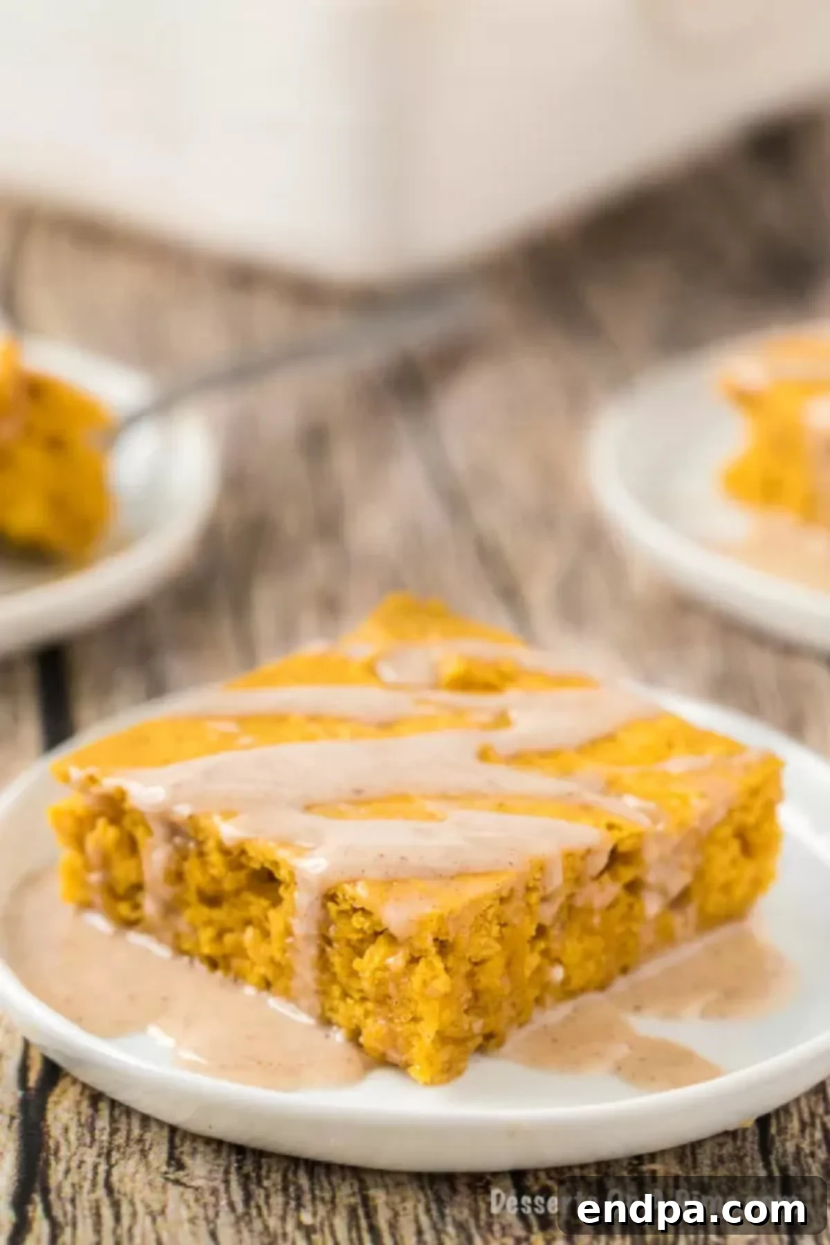 A perfectly sliced piece of pumpkin cake drizzled with glaze, served on a white plate, ready to be enjoyed.