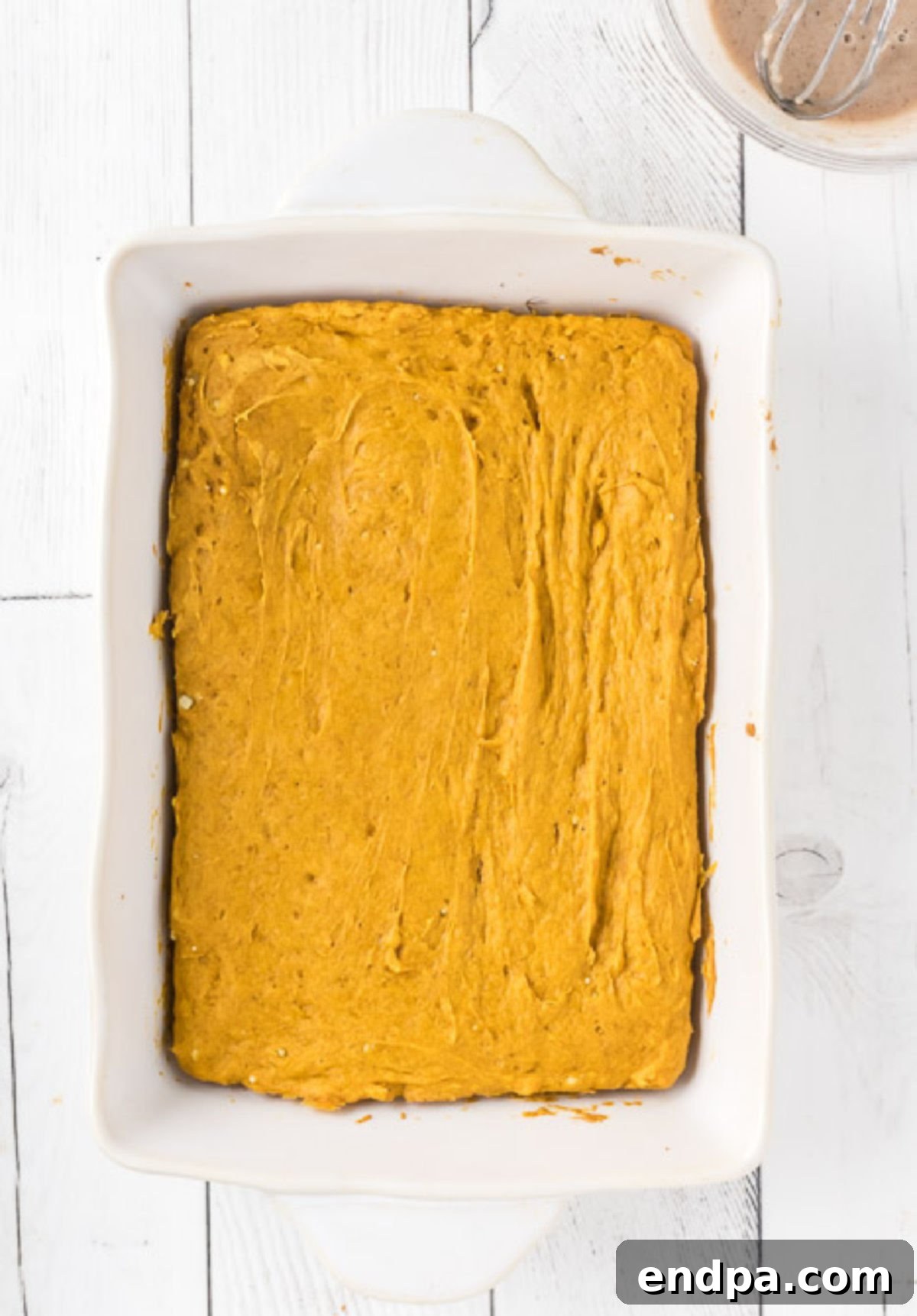 The pumpkin cake batter evenly spread in a baking dish, ready for the oven.