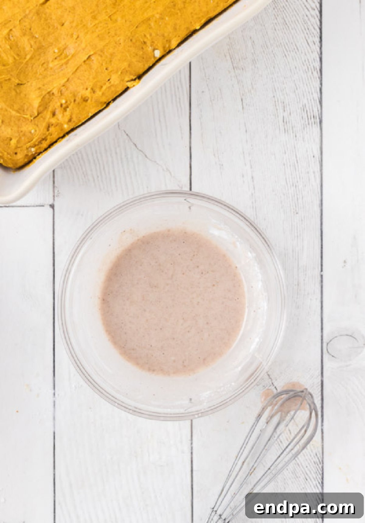 Powdered sugar, apple juice, and pumpkin pie spice mixed together in a small bowl, forming a smooth, pourable glaze.