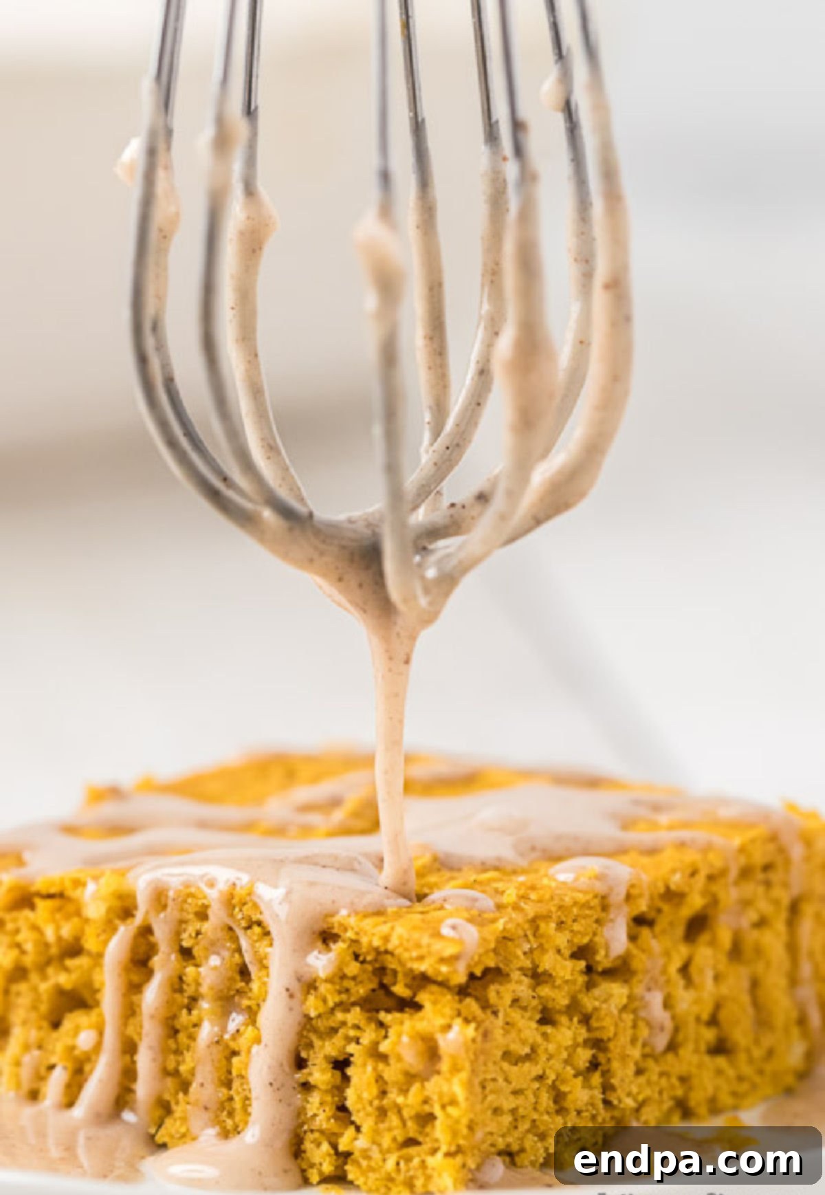 The pumpkin pie spice glaze being artfully drizzled over the top of the cooled, golden pumpkin cake in a baking dish.