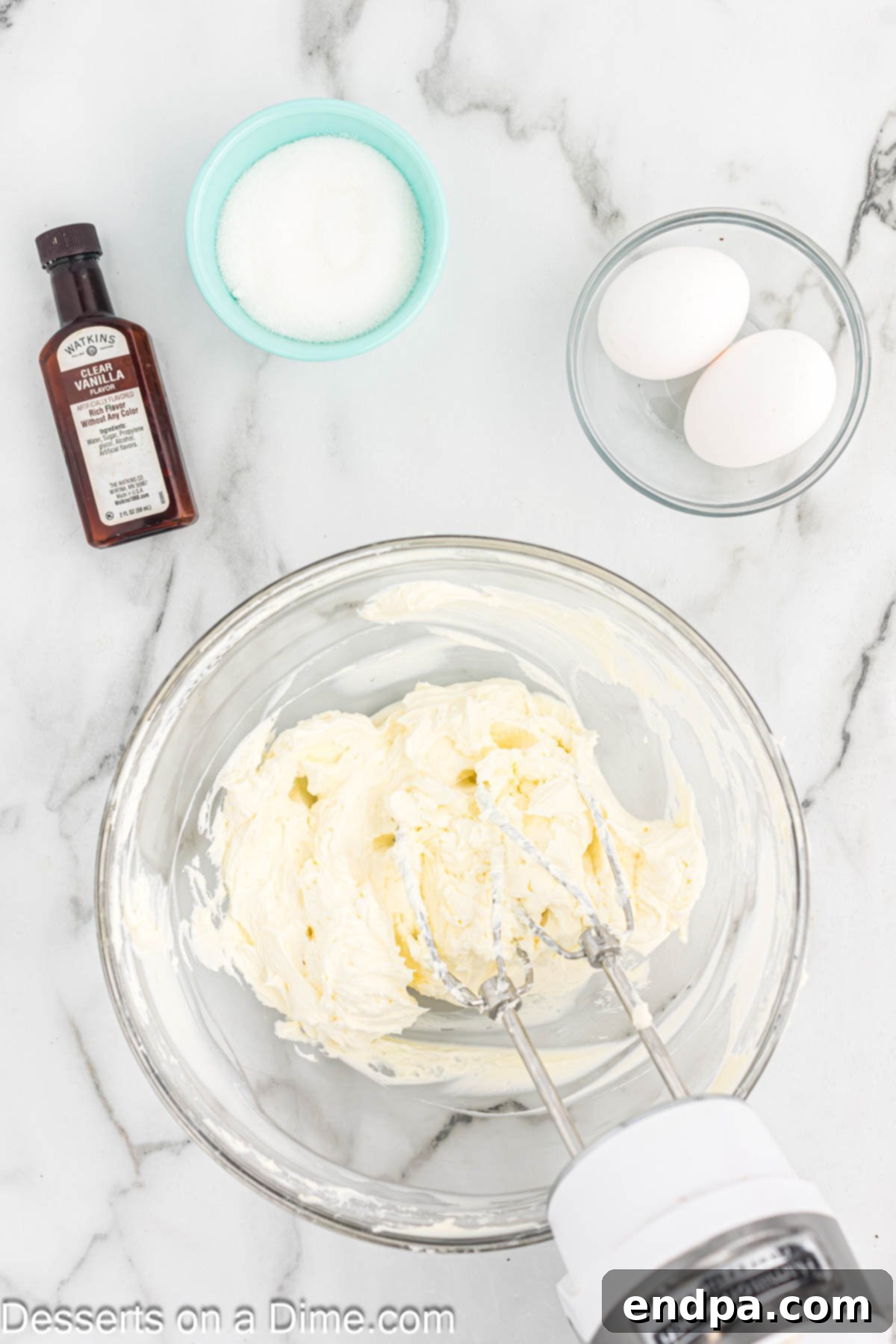 Softened cream cheese being beaten in a mixing bowl with an electric mixer until smooth.