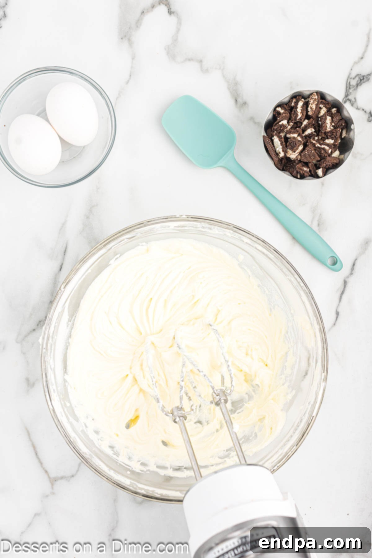 Granulated sugar and vanilla extract being added to the creamed cream cheese in a mixing bowl.