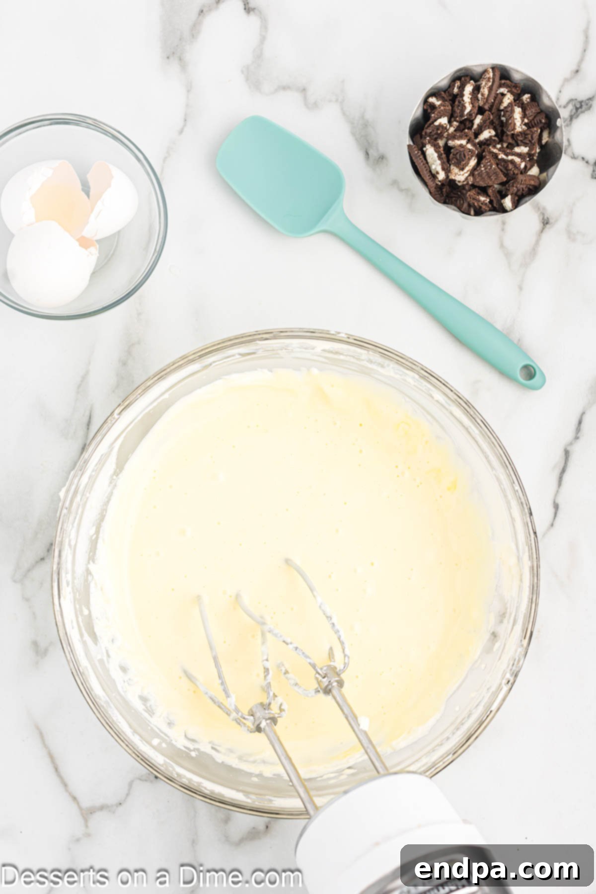 Eggs being added one at a time to the cheesecake batter in a mixing bowl.