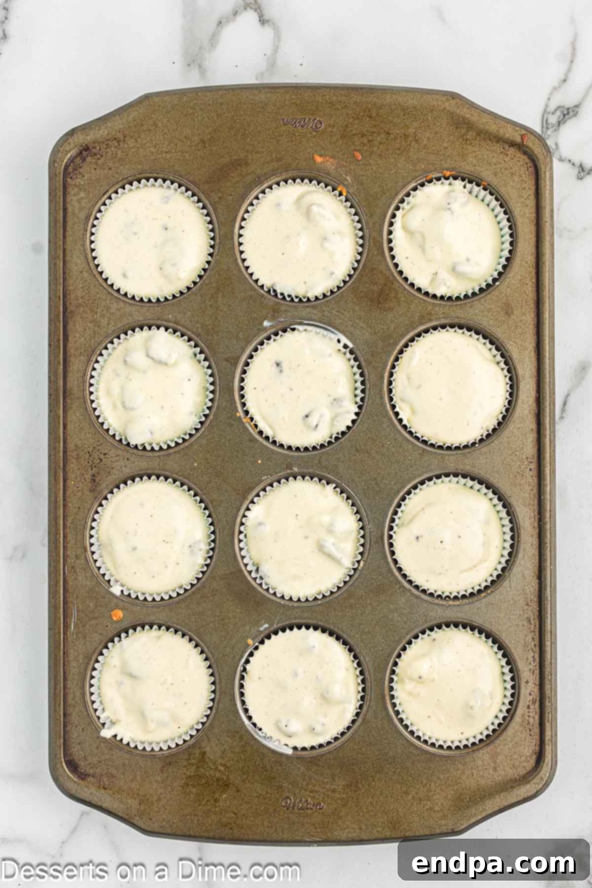 Cheesecake batter with Oreo pieces being poured into muffin tins lined with whole Oreos.