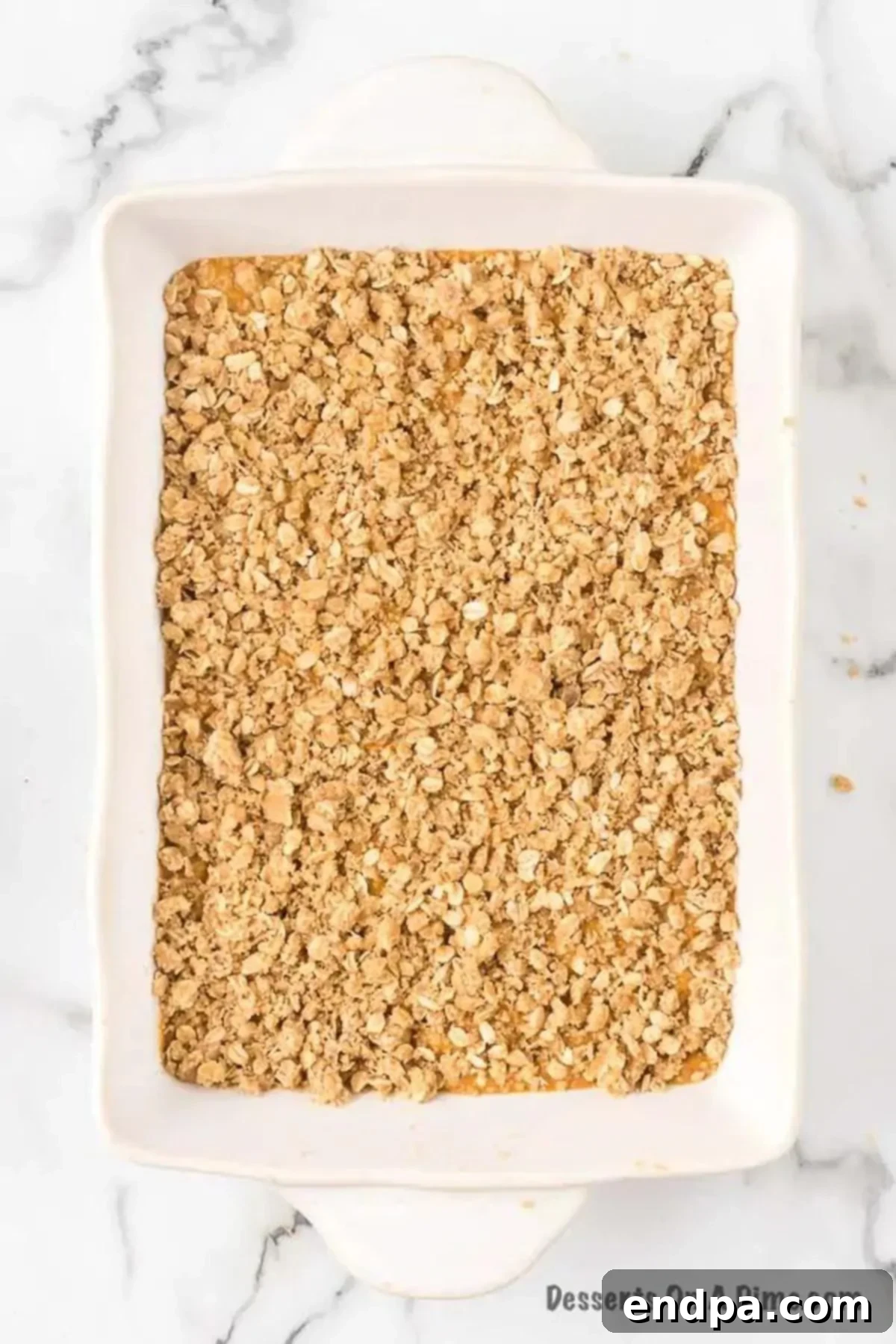 Autumn Pumpkin Crumble 7 Crumbly oat topping being sprinkled generously over the pumpkin layer in the baking dish.
