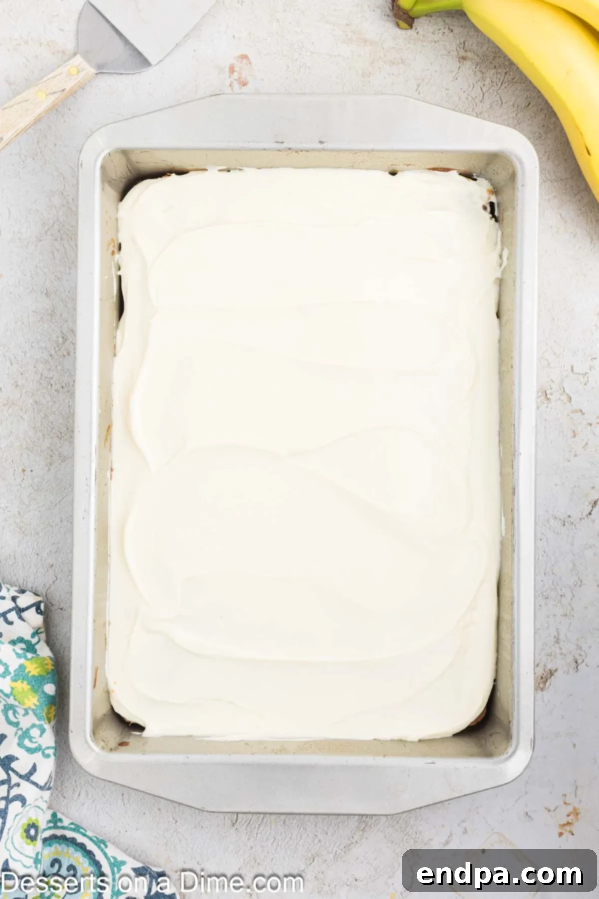 Ultimate Banana Bars 10 Cream cheese frosting being spread smoothly and evenly over the cooled banana bars in the pan.